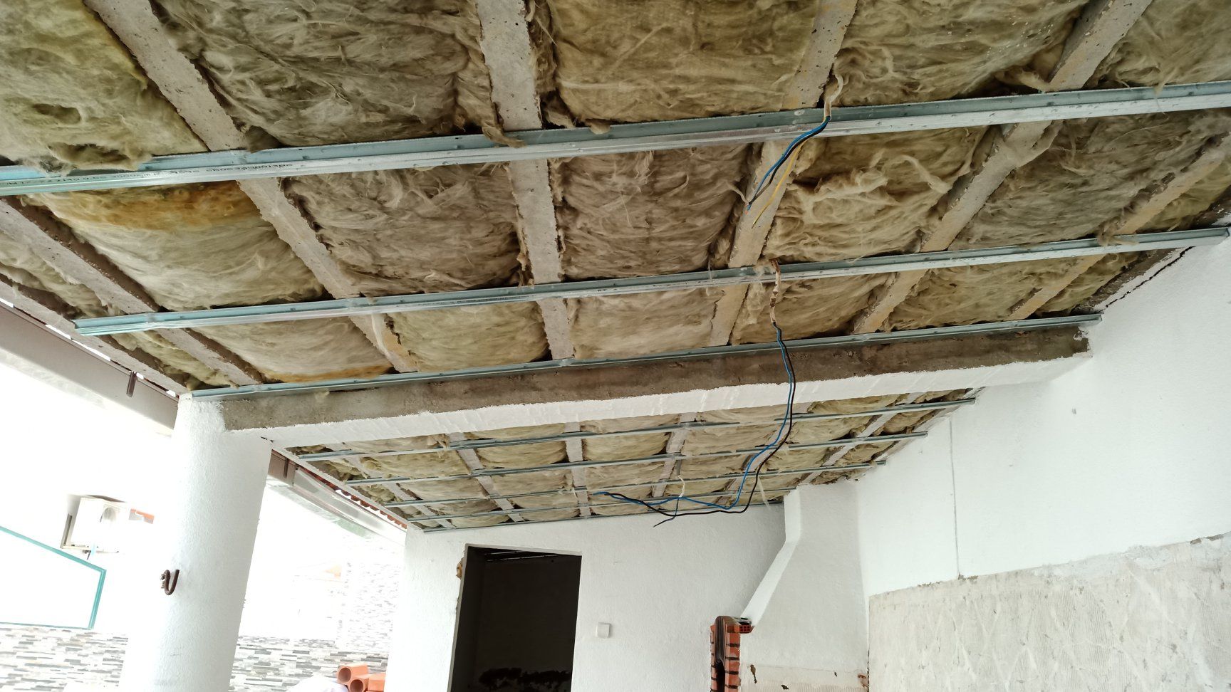 Isolamento instalado no teto, com estrutura metálica exposta e fiação visível.