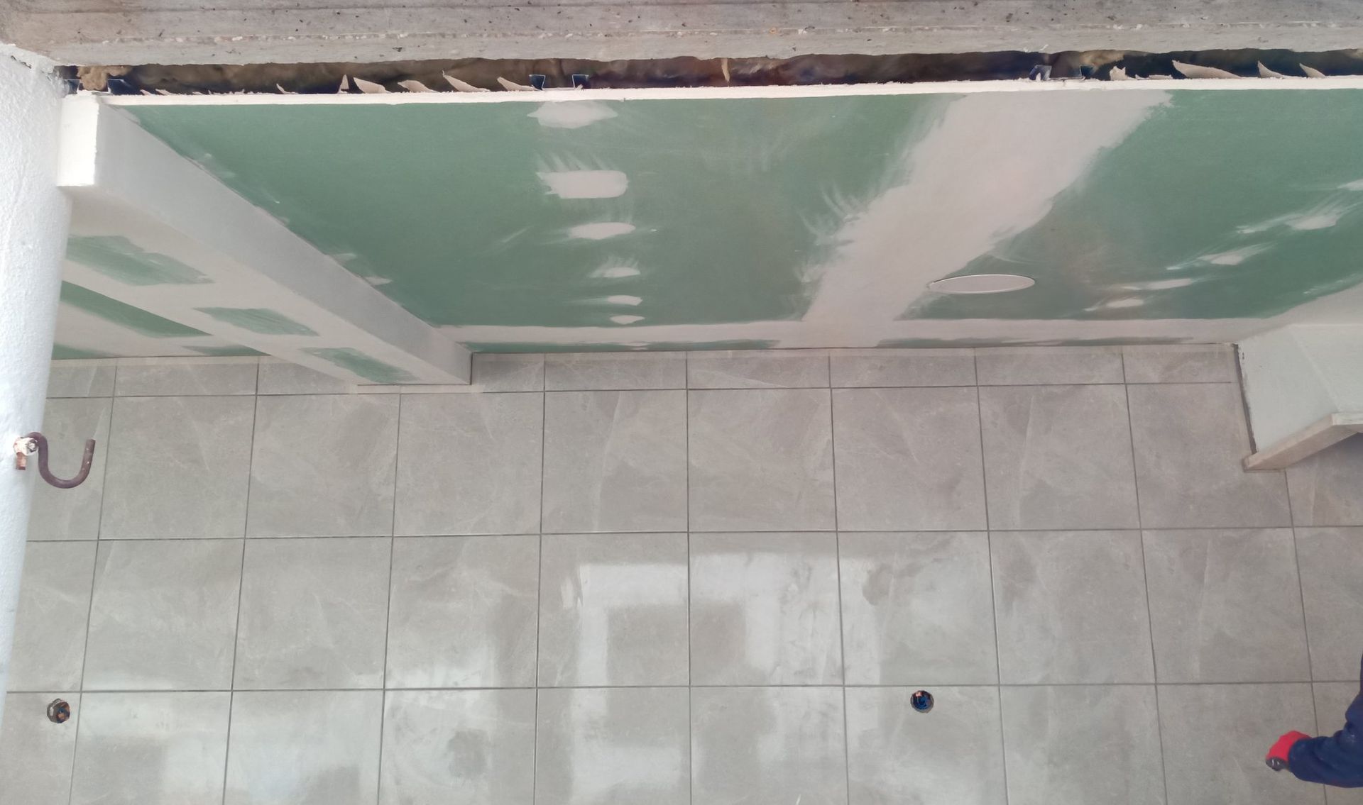Quarto em construção, com piso de azulejo e teto de gesso acartonado verde parcialmente instalados.
