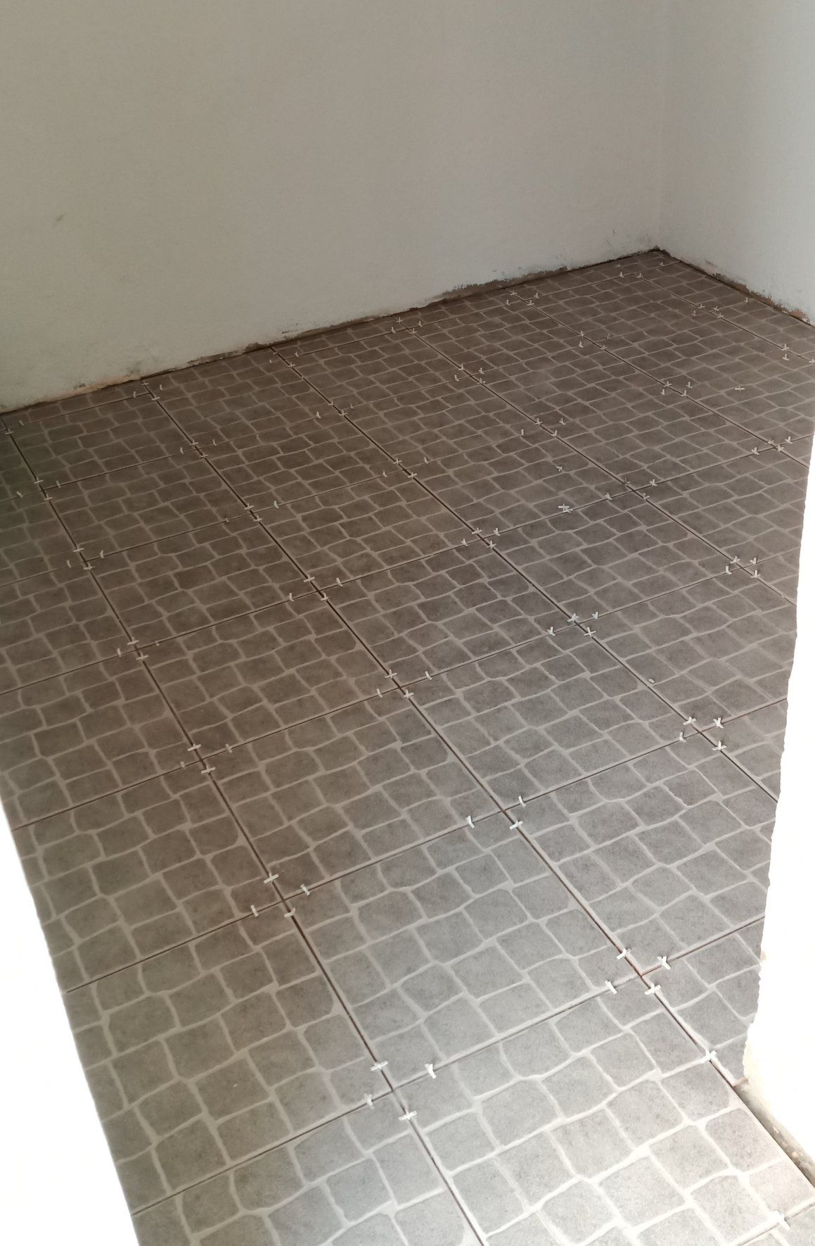 Piso de azulejo em um cômodo com luz vinda da direita, paredes brancas.