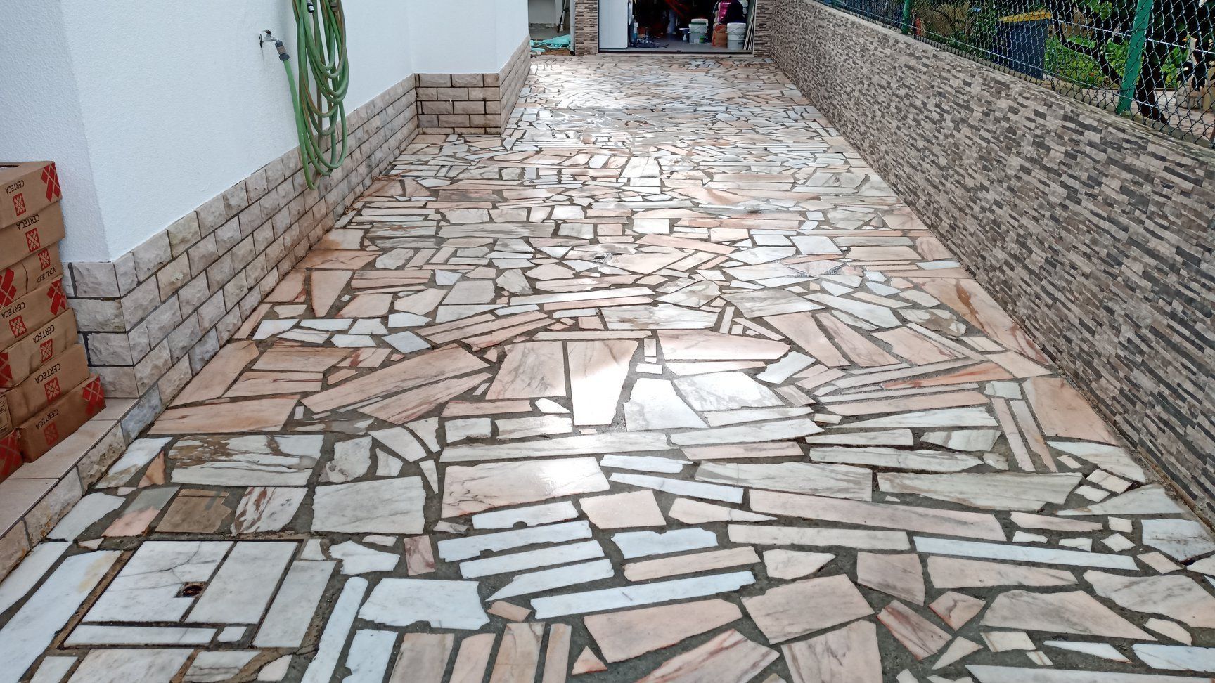 Caminho pavimentado com pedras irregulares bege e cinza, delimitado por muros de pedra, que leva a uma abertura.