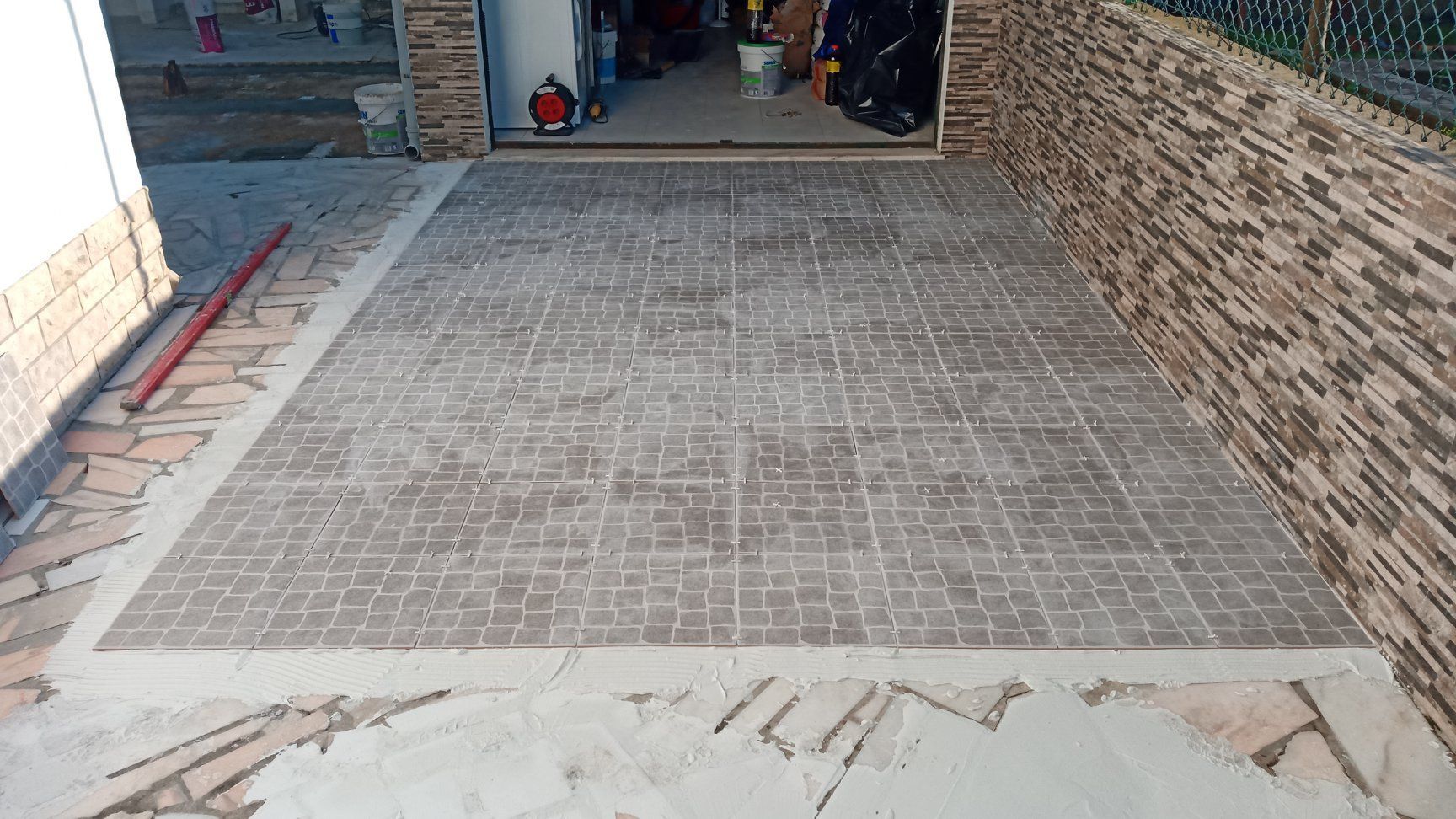 Hall de entrada recém-revestido com azulejos em padrão de mosaico, ao lado de uma parede de tijolos texturizados e da garagem.