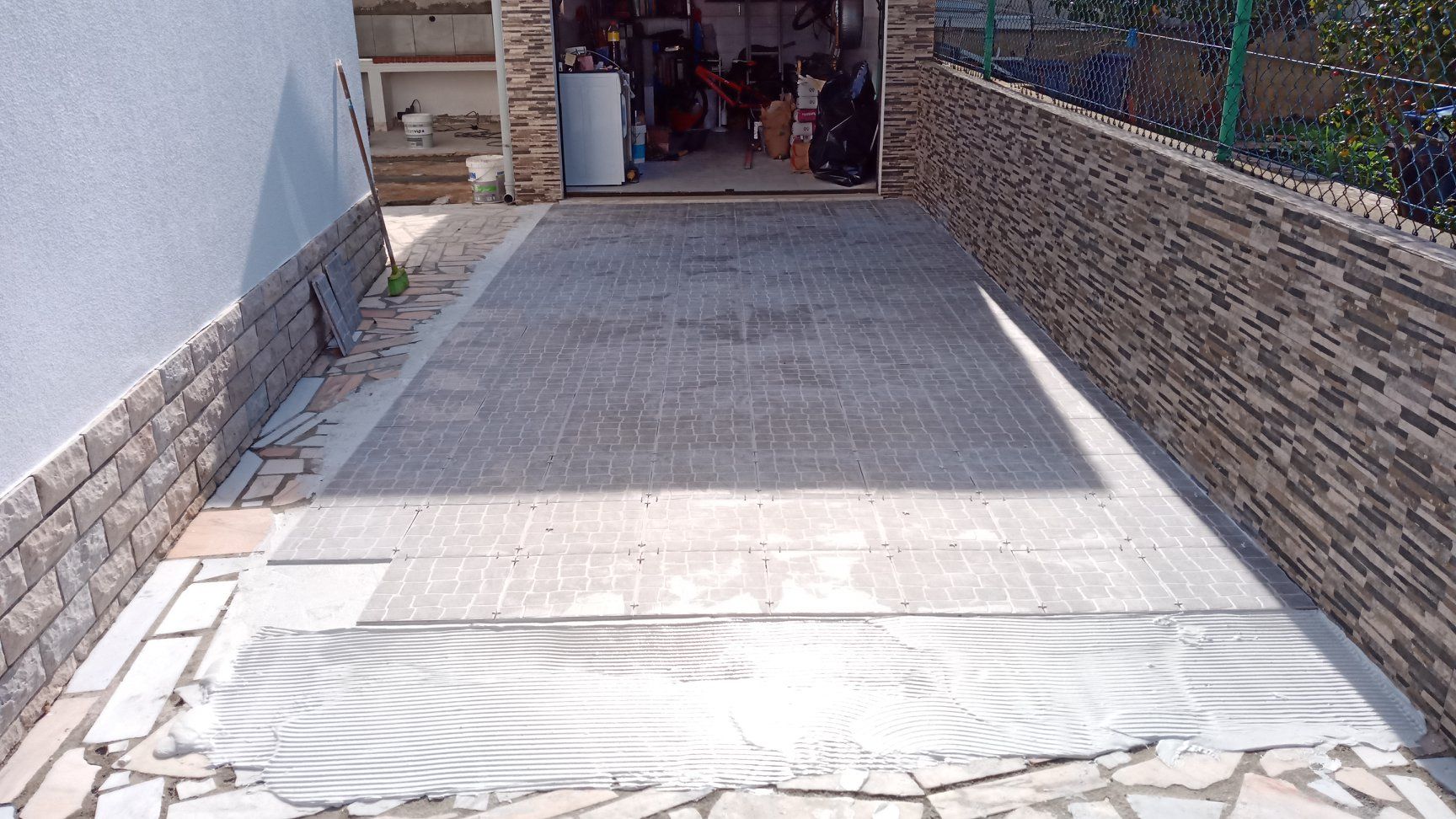 Entrada de automóveis em concreto que leva a uma garagem aberta; paredes de tijolos em ambos os lados.