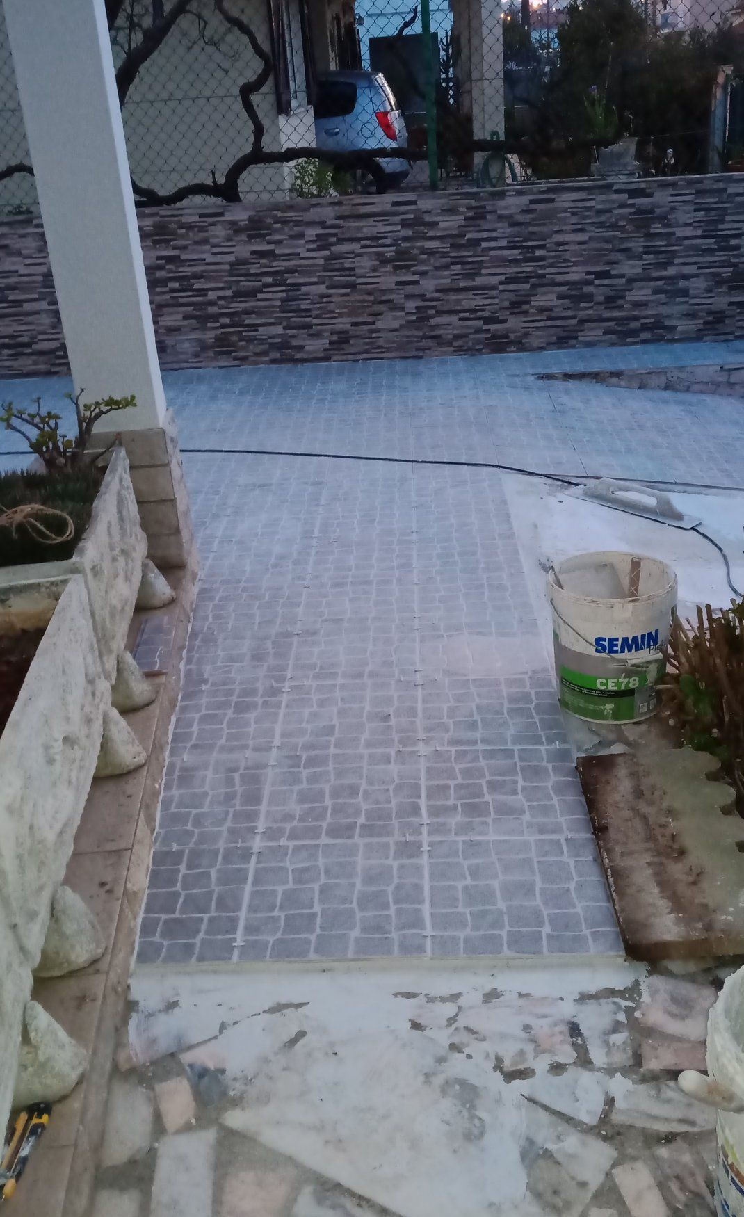 Uma passarela de azulejos que leva a uma casa com um muro de pedra e um balde.