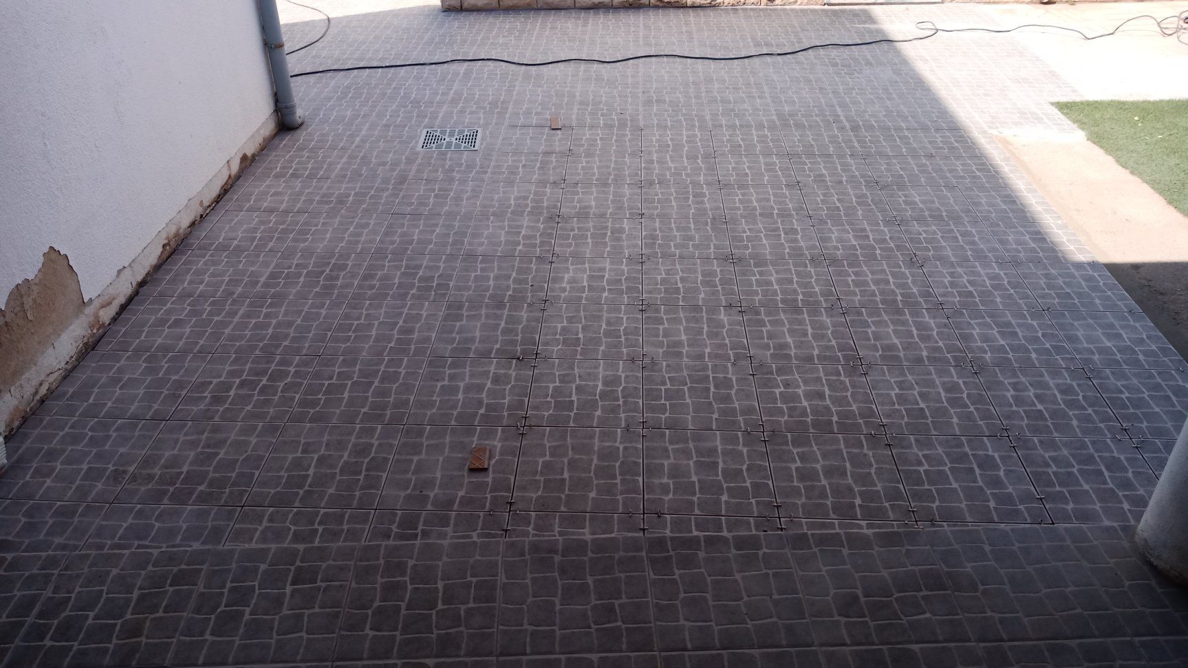 Pátio de tijolos rachados com uma parede rachada. Luz solar direta projetando sombras.