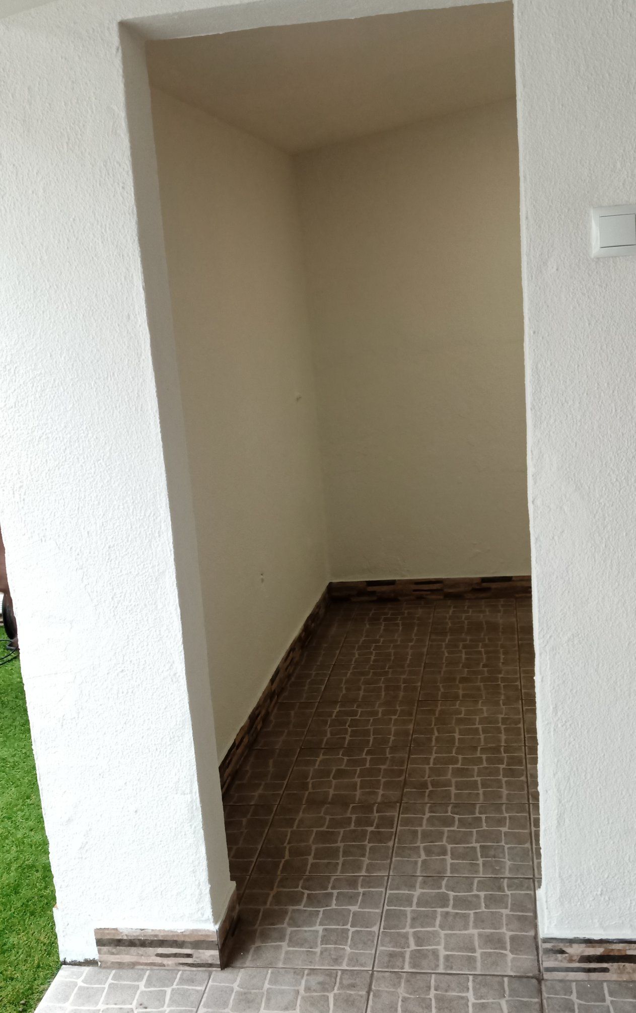 Nicho vazio com piso de azulejo e paredes em tom creme, visto de uma entrada com estuque branco.