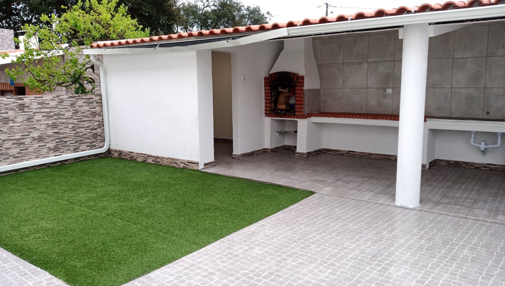 Área de cozinha externa com grama artificial e churrasqueira embutida.
