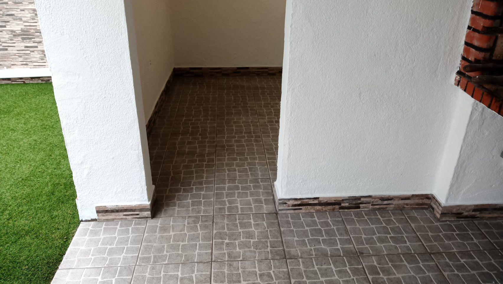 Área externa coberta com piso de azulejo, paredes brancas e alvenaria à direita.