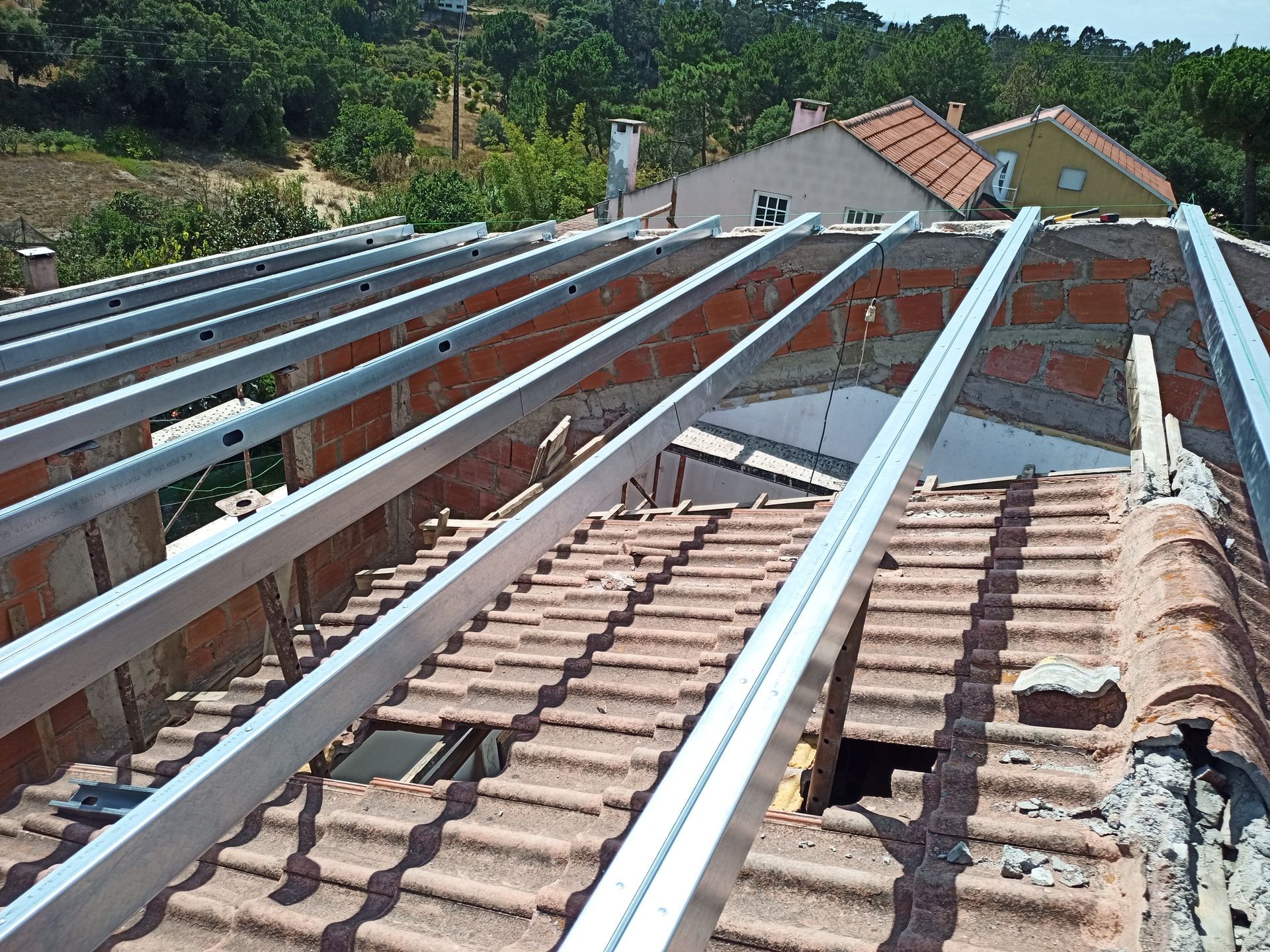 Telhado com telhas vermelhas e estruturas de suporte metálicas, preparado para instalação de painéis solares, sob um céu claro.