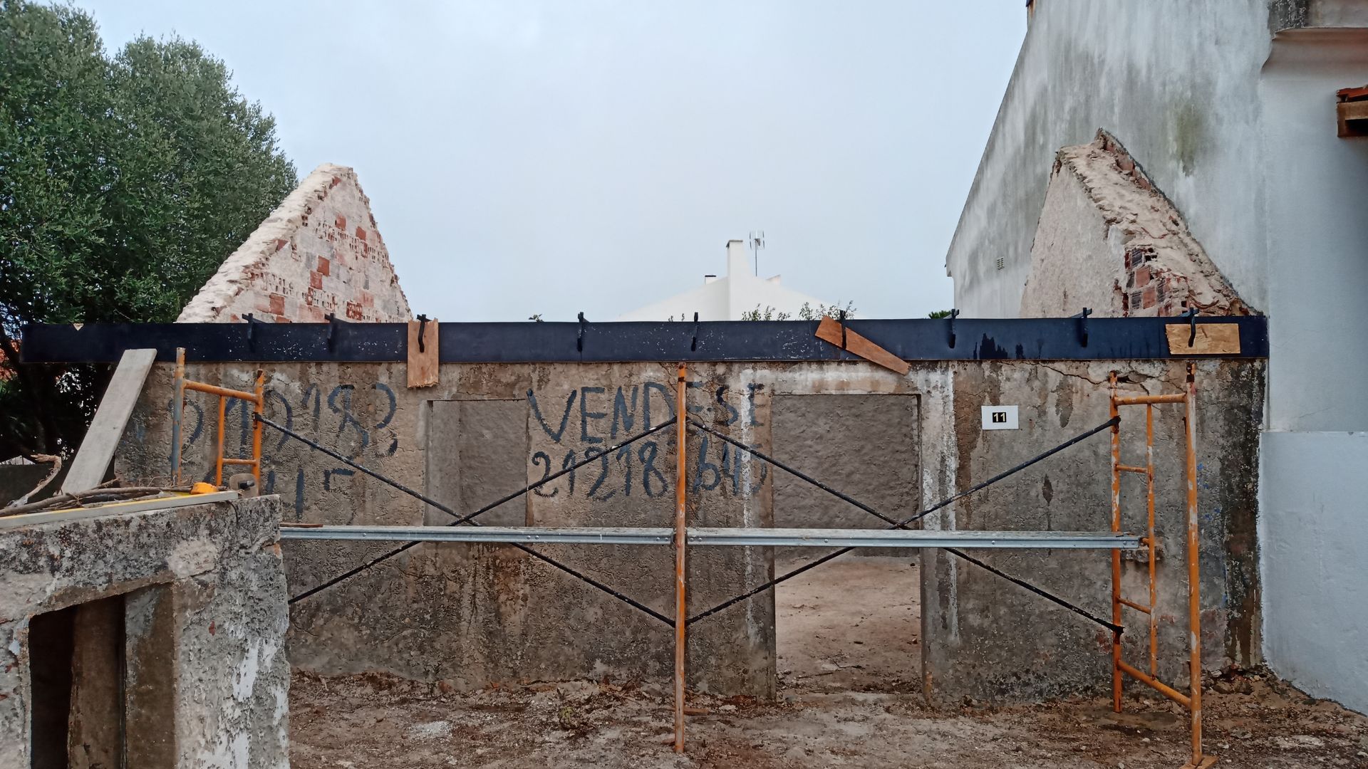 Exterior de um edifício em construção, com paredes de concreto, andaimes e a inscrição visível 