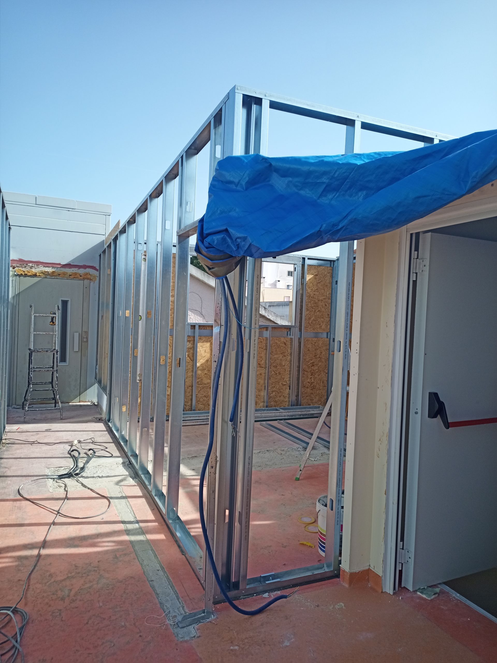 Estrutura metálica de um edifício em construção, com lona azul por cima e interior exposto.