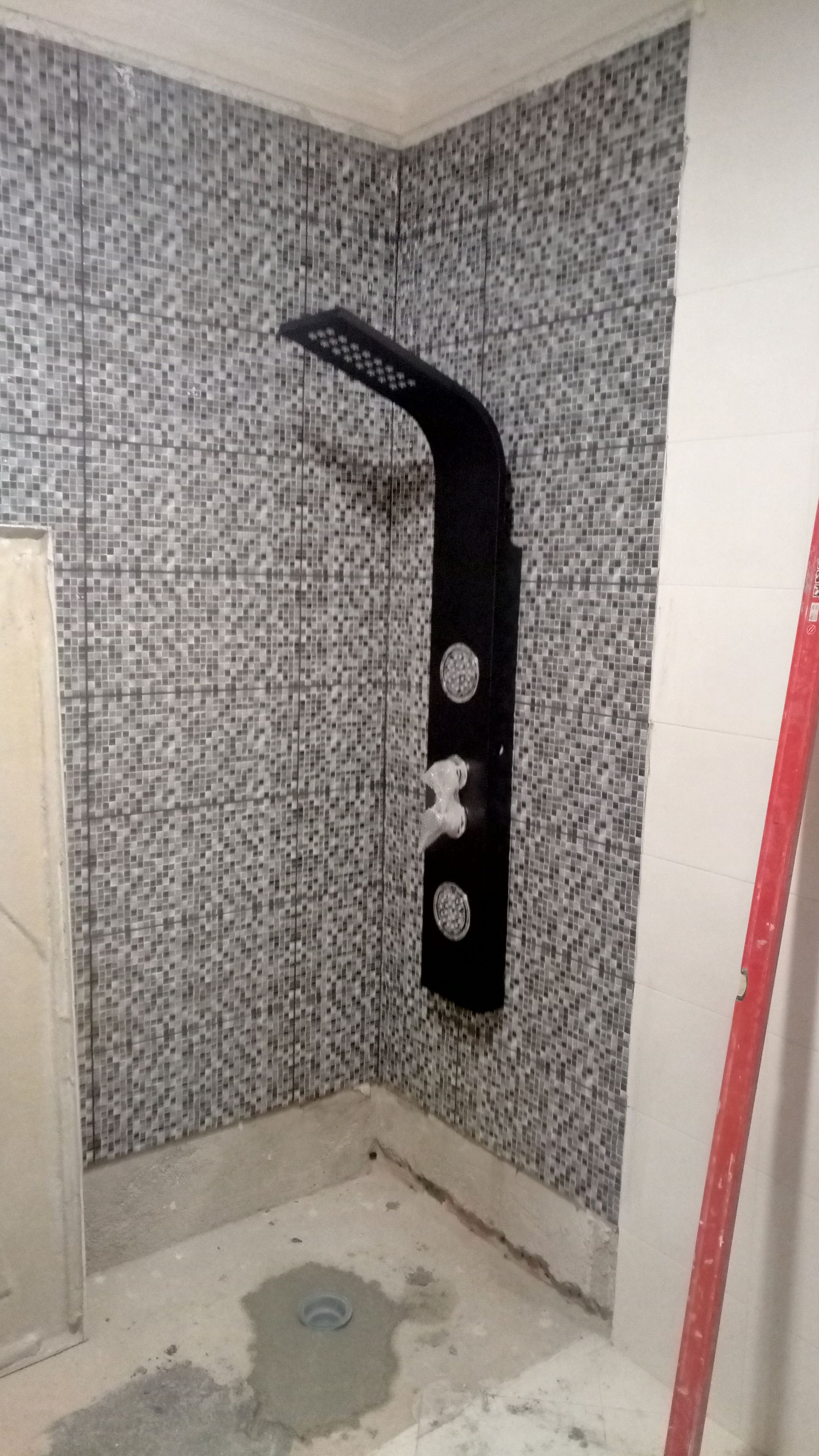 Painel de chuveiro preto instalado em uma parede revestida com azulejos em um banheiro em construção.