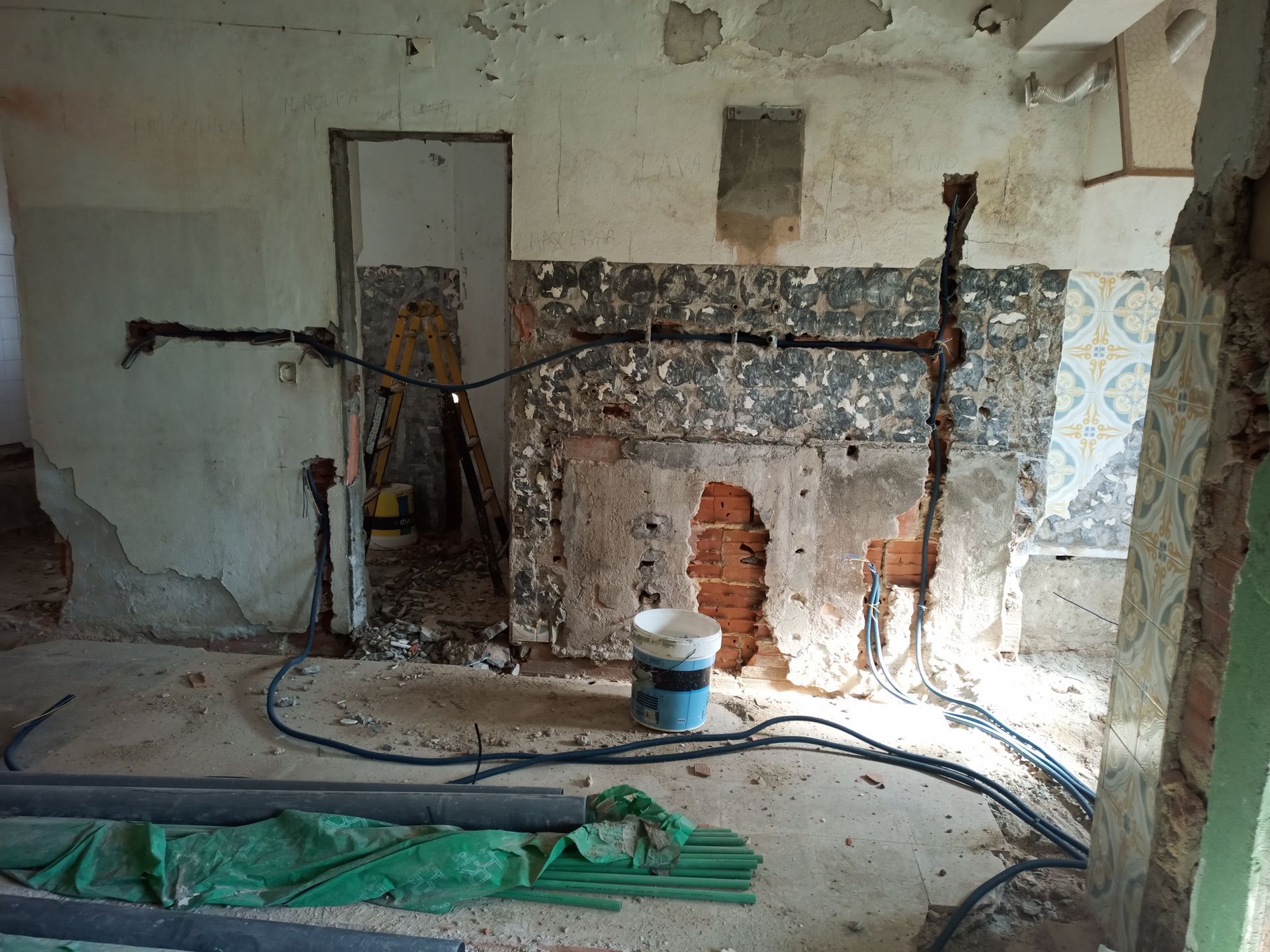 Quarto em reforma com tijolos aparentes, restos de azulejos, fiação elétrica e entulho.