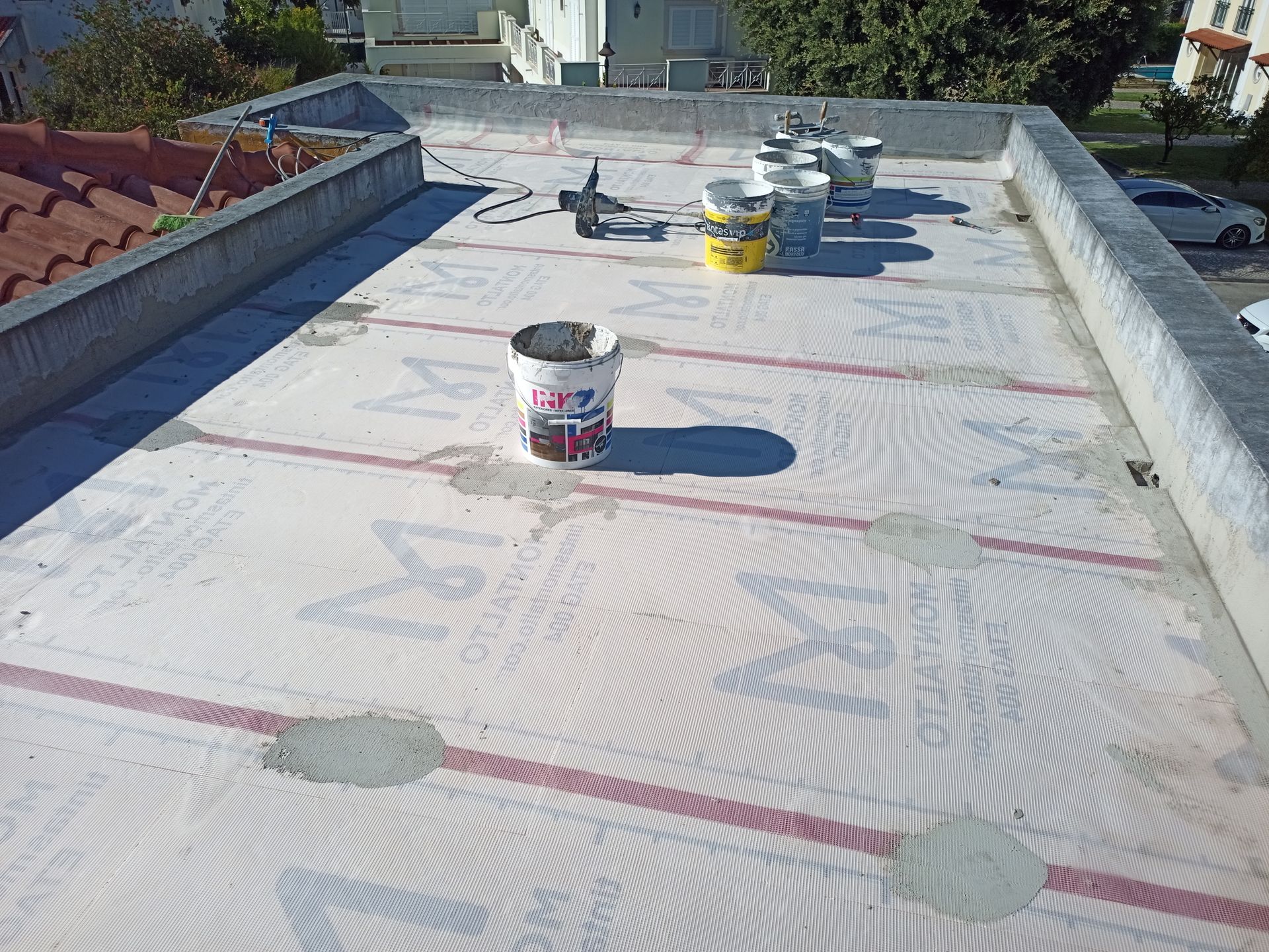 Telhado plano com baldes, possivelmente em construção, bordas de concreto cinza, superfície clara com linhas vermelhas.