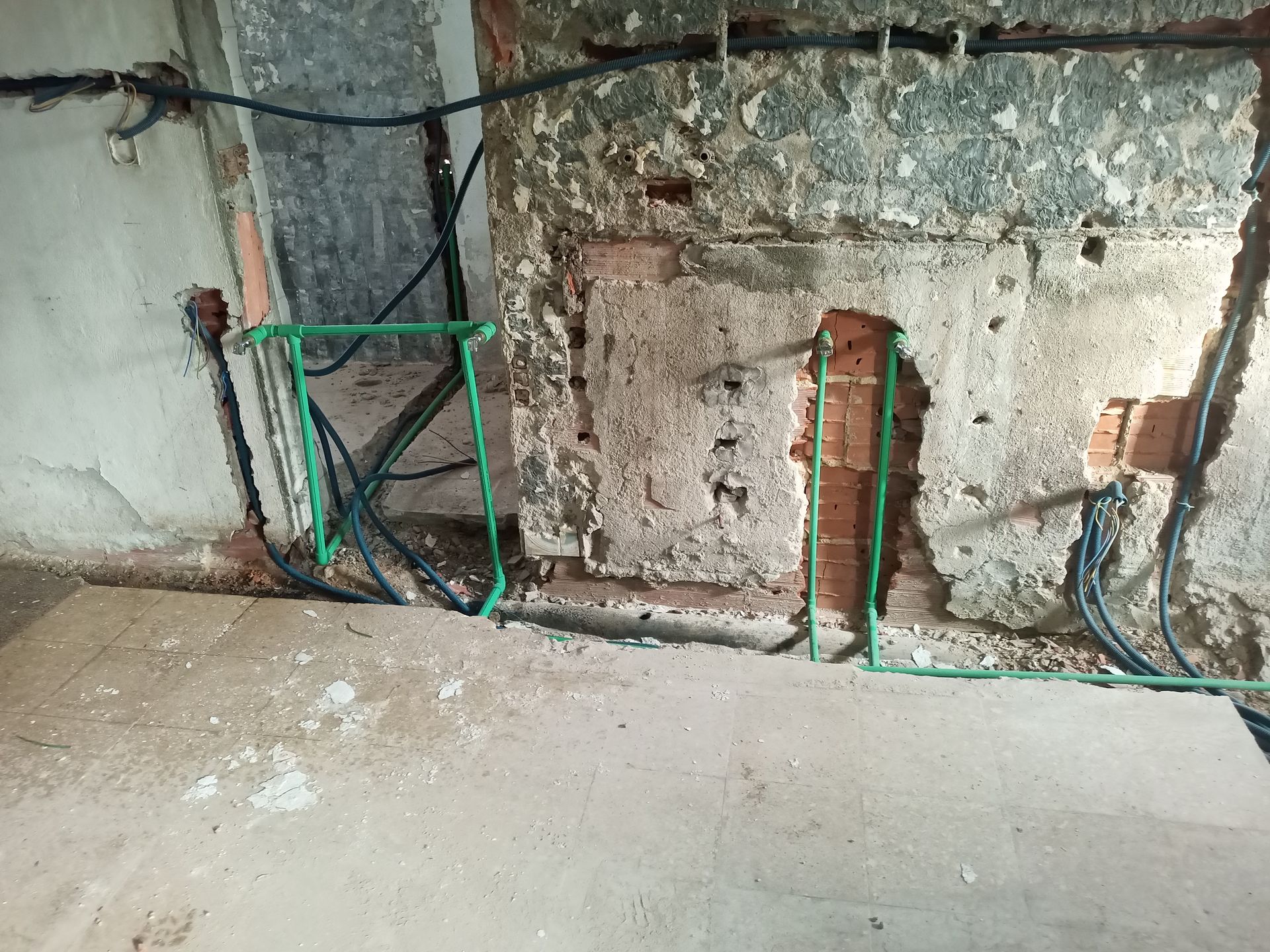 Tubulações de encanamento verdes e fiação elétrica em uma abertura na parede; construção em andamento.