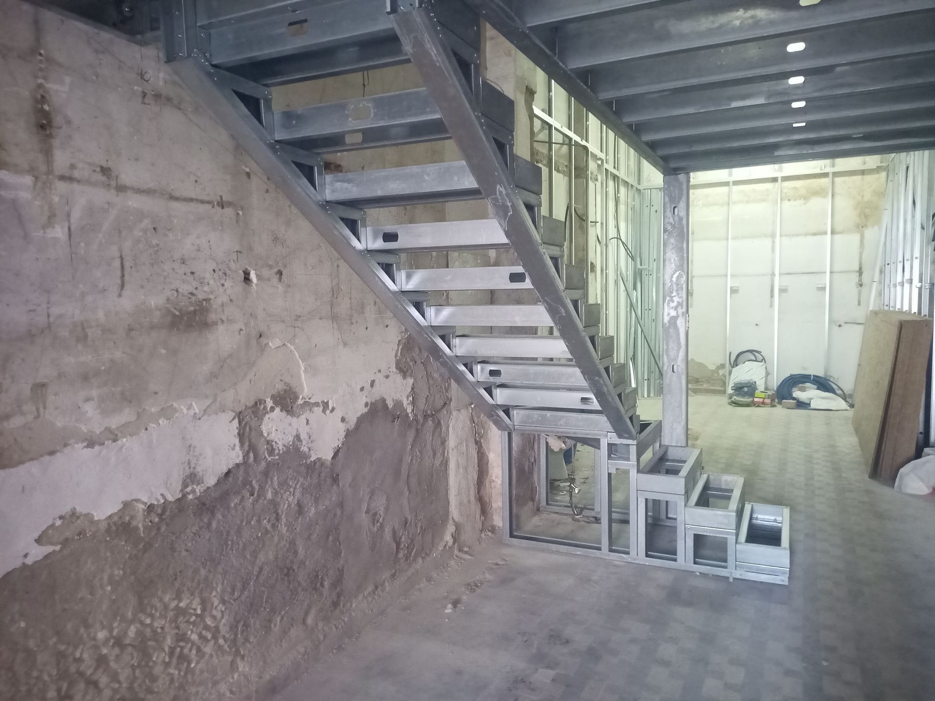 Escada metálica em construção em um prédio com paredes de concreto e um corredor.
