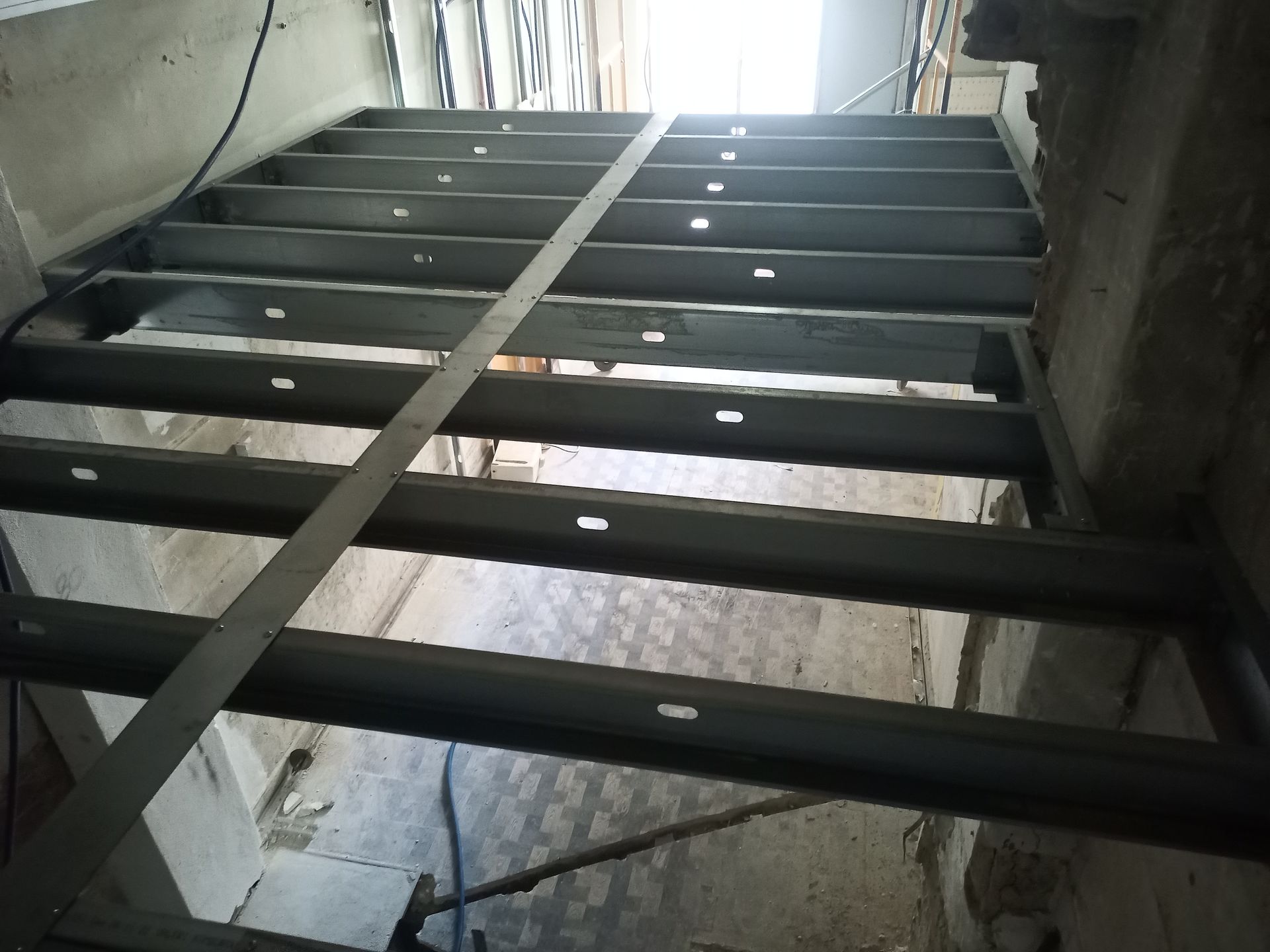 Escada metálica com degraus vazados, subindo em direção à luz. Canteiro de obras.