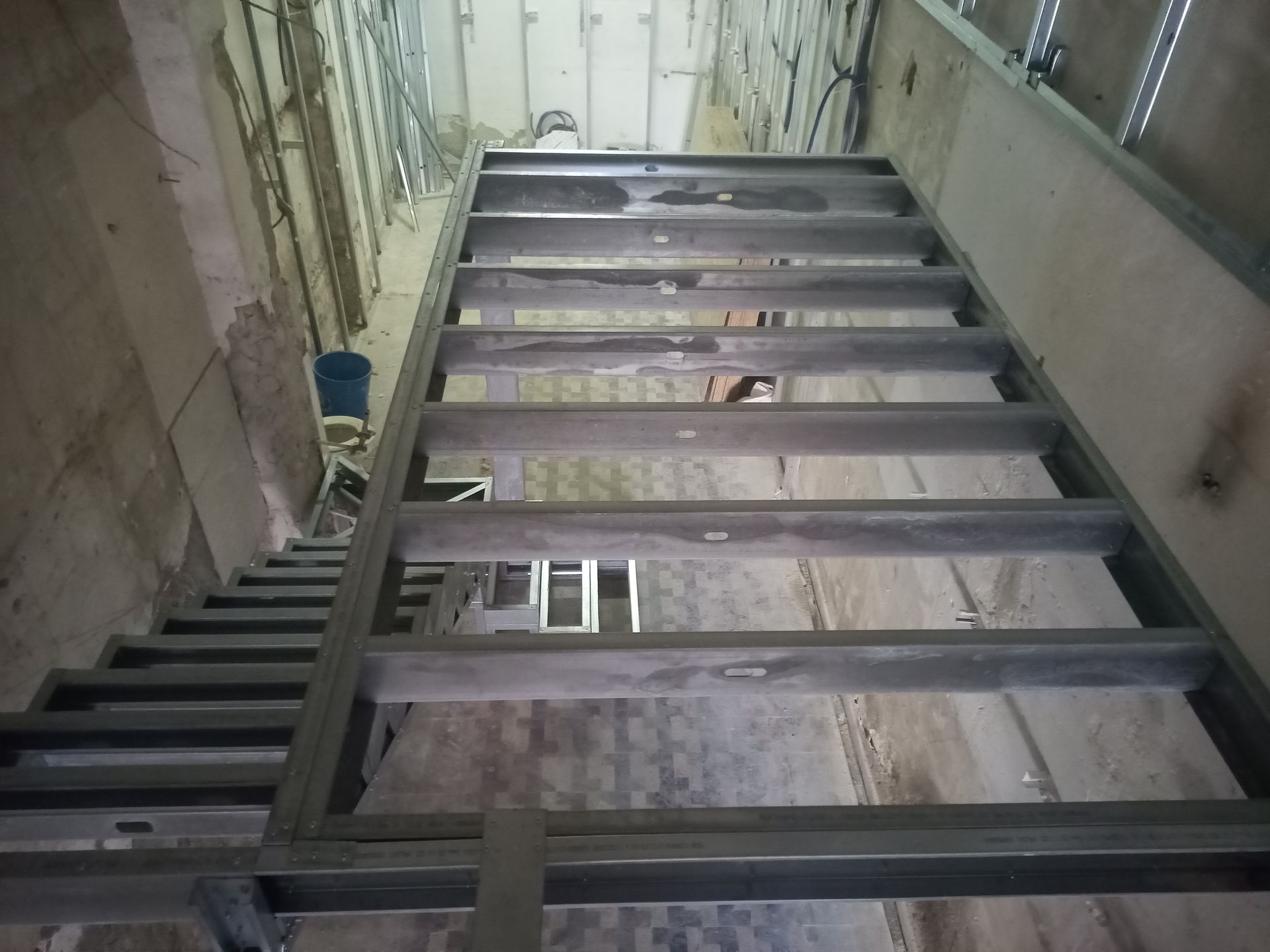 Escada metálica em construção, dentro de um edifício. Os degraus são cinza. Fios e componentes elétricos estão visíveis.