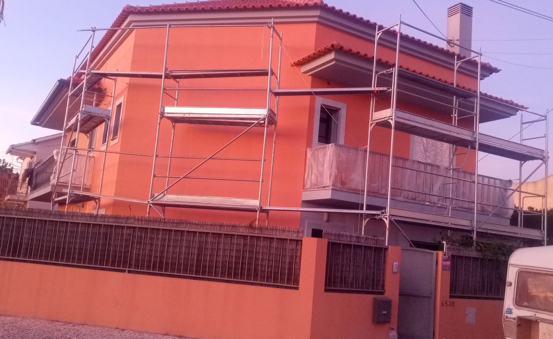Casa laranja em reforma, cercada por andaimes. Cerca marrom na frente.