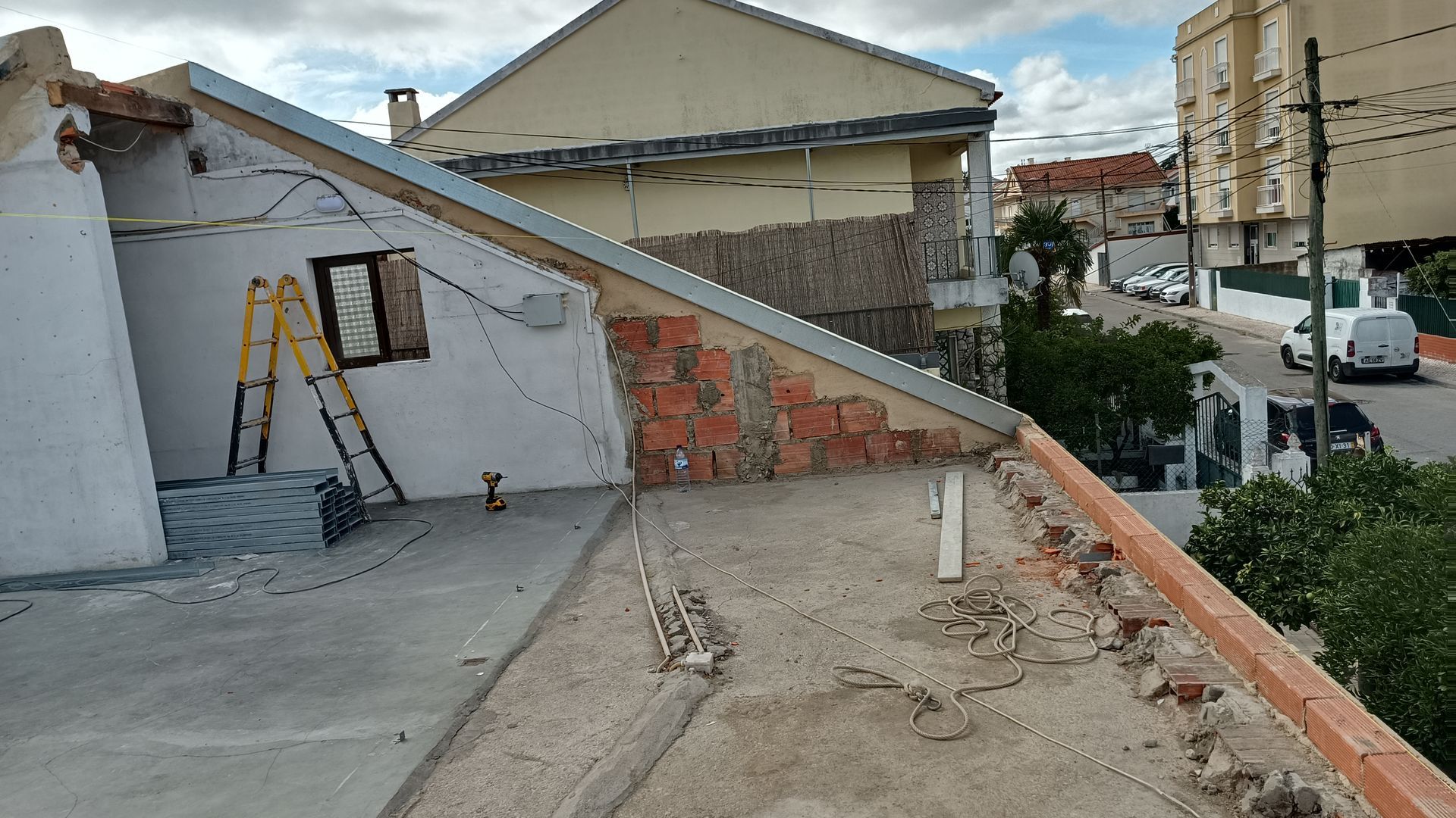 Telhado em construção com tijolos aparentes, escadas e prédios ao redor sob céu nublado.