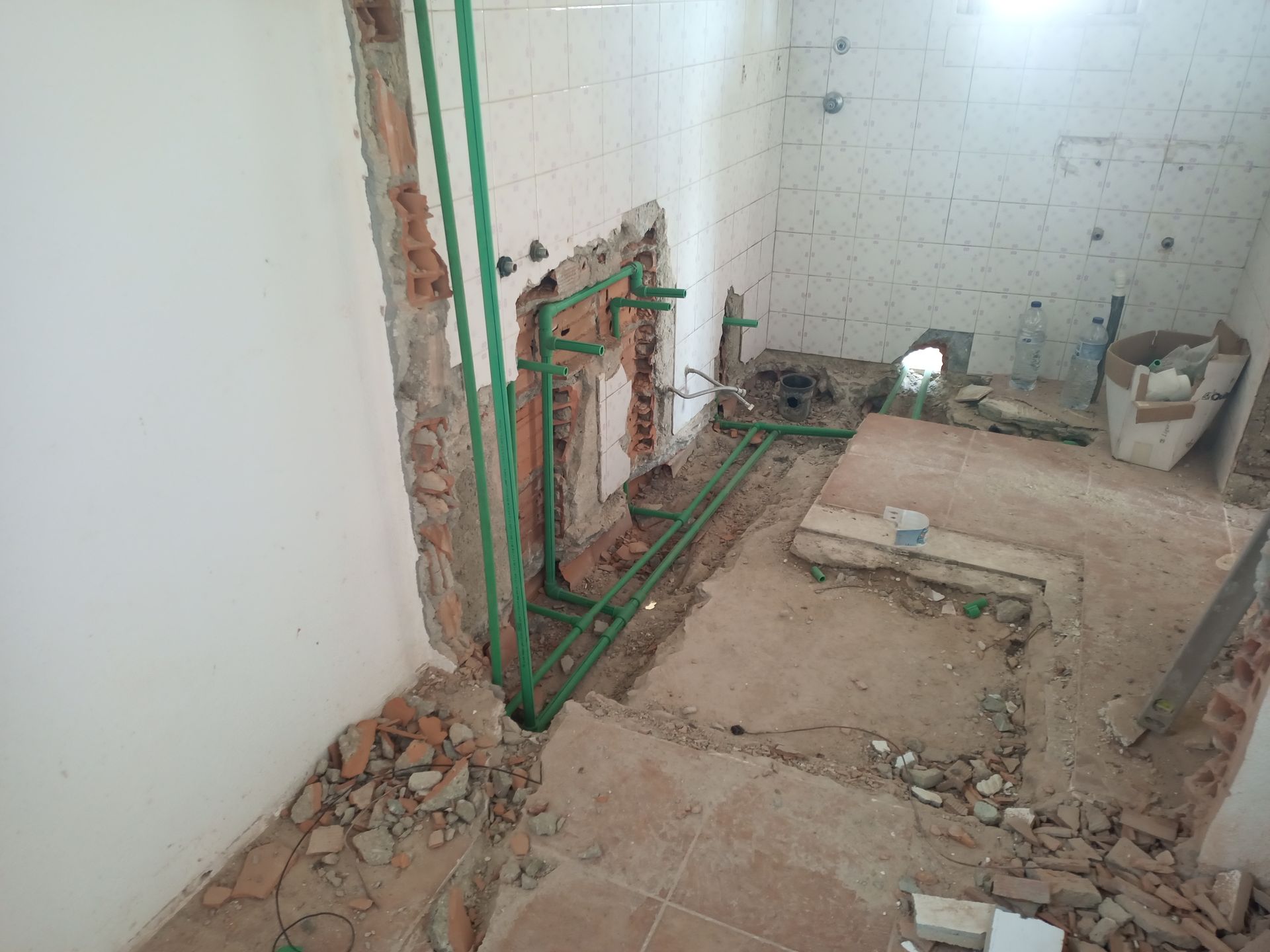 Banheiro em construção com canos verdes expostos e entulho.