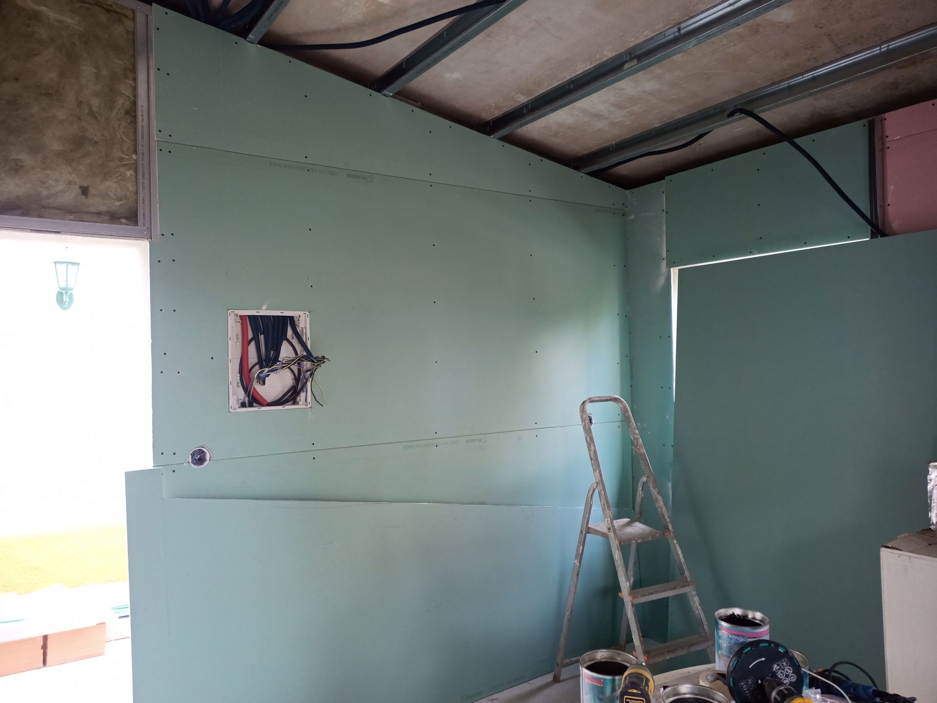 Construção interna: drywall verde parcialmente instalado sobre os montantes; escada, latas de tinta.