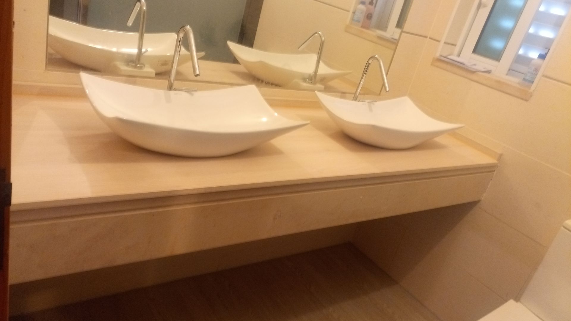 Duas cubas de apoio brancas sobre uma bancada de mármore com torneiras cromadas em um banheiro.