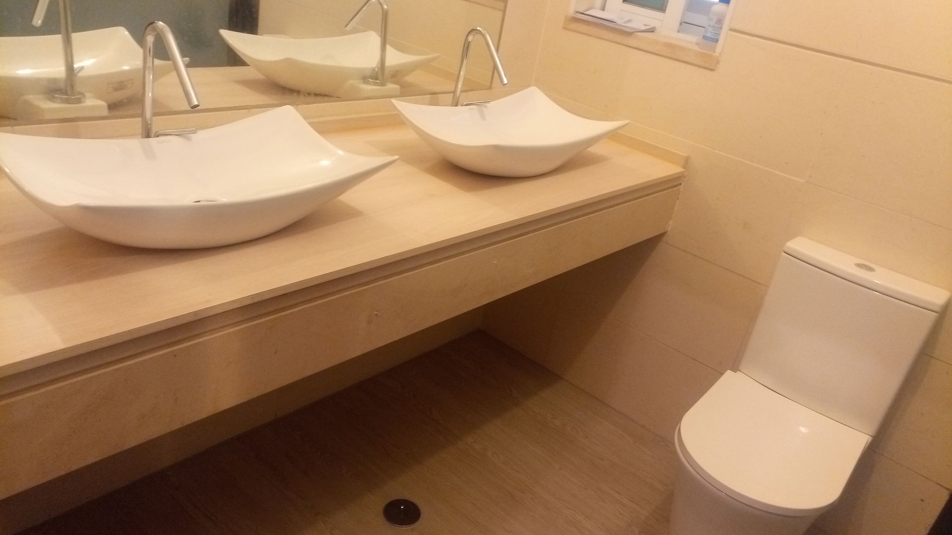 Banheiro com duas pias brancas sobre uma bancada de madeira e um vaso sanitário branco.