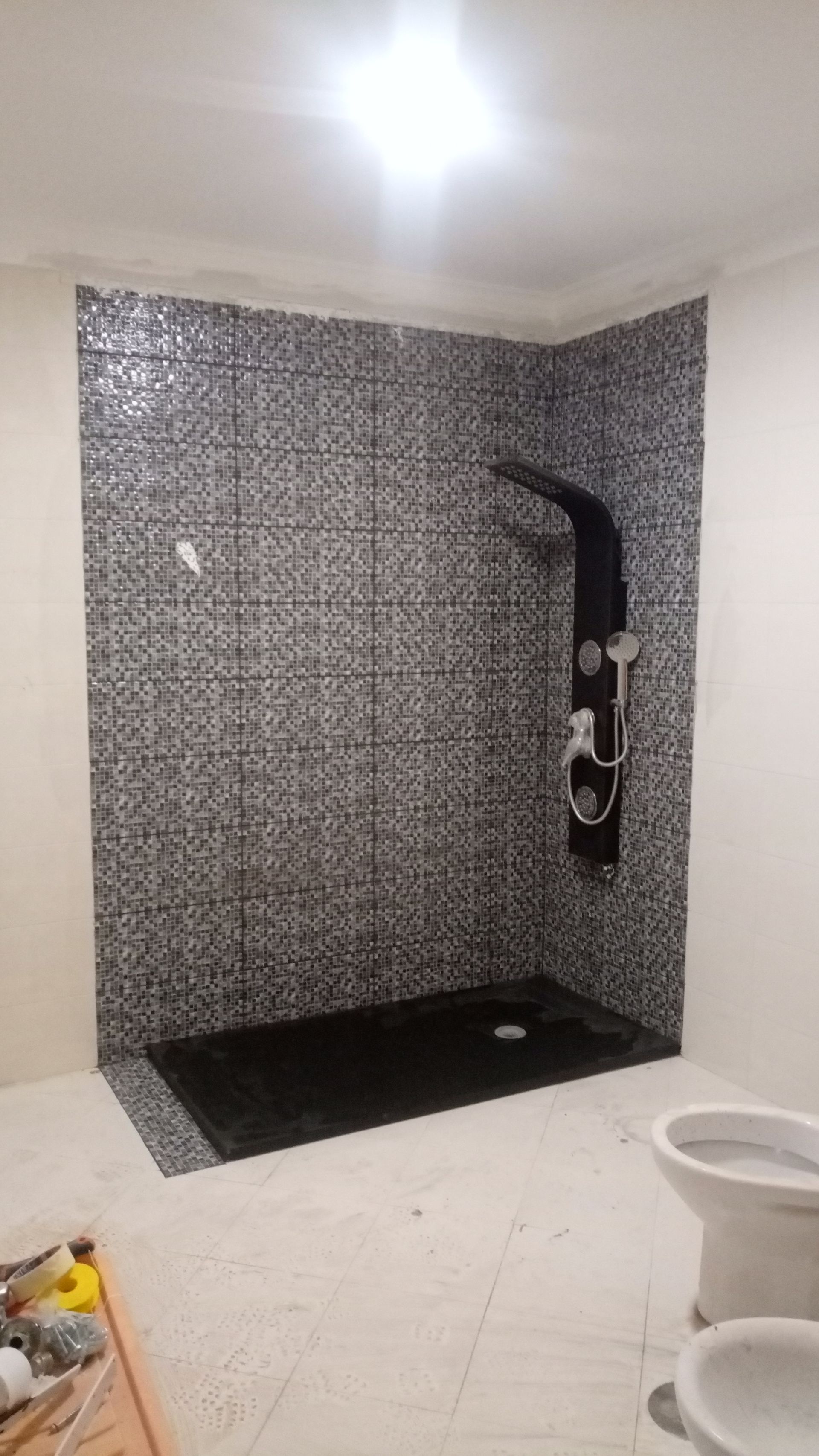 Box de chuveiro revestido com azulejos pretos, com acessórios e base também pretos, recém-instalado.