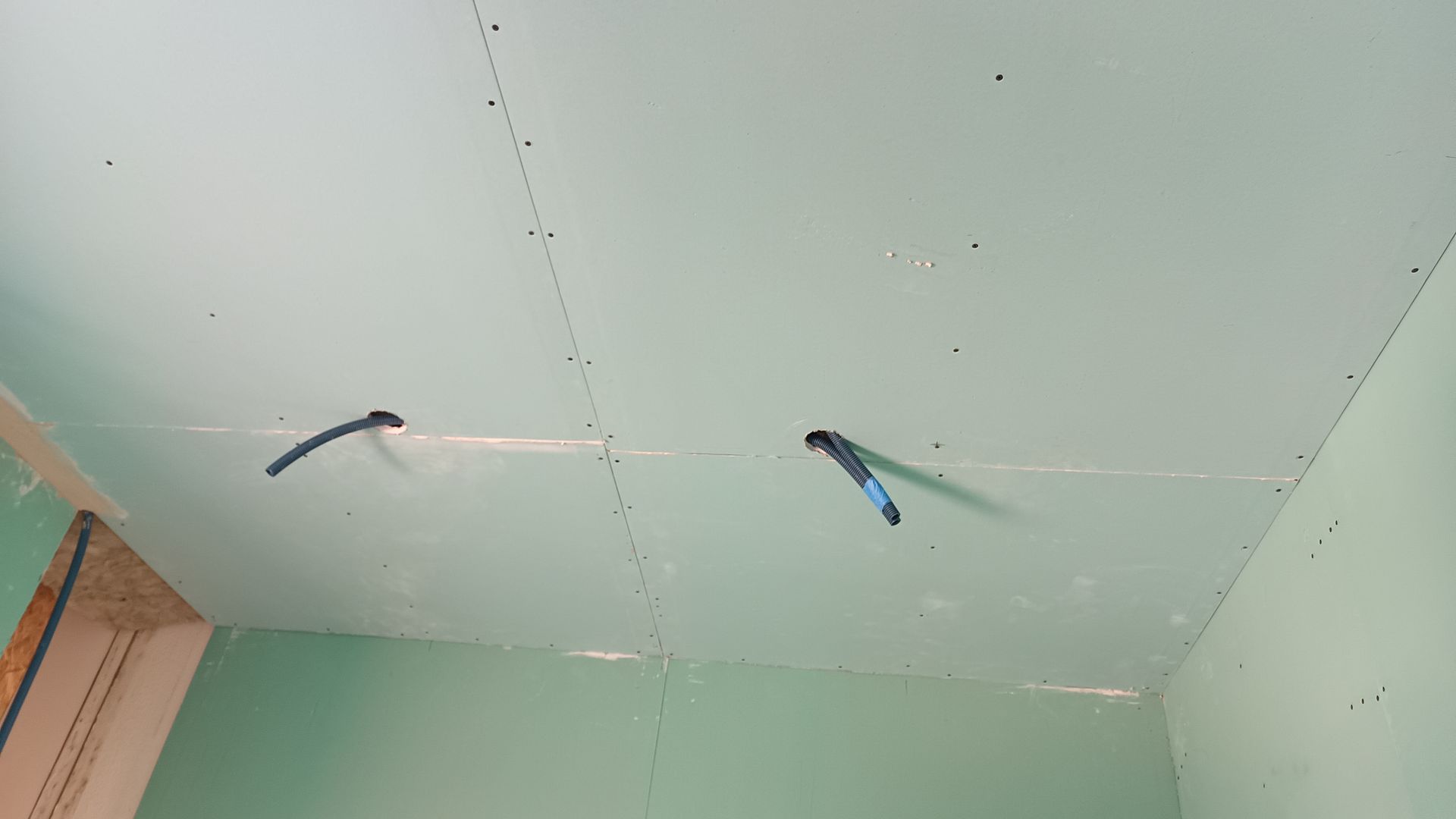Teto com drywall instalado, fiação elétrica e juntas visíveis. Paredes verdes em um cômodo.