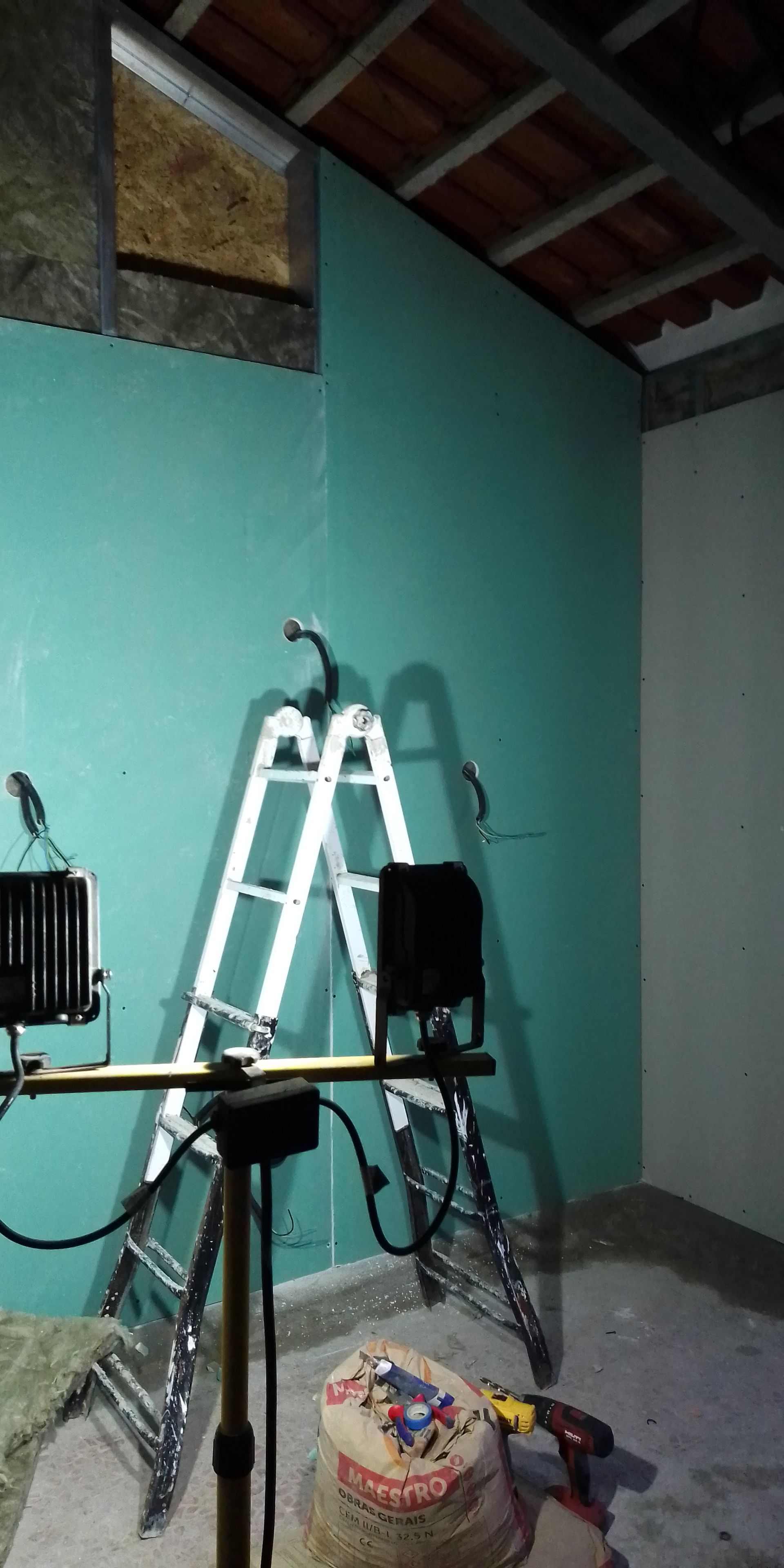 Um cômodo em construção com uma escada, ferramentas e uma parede verde.