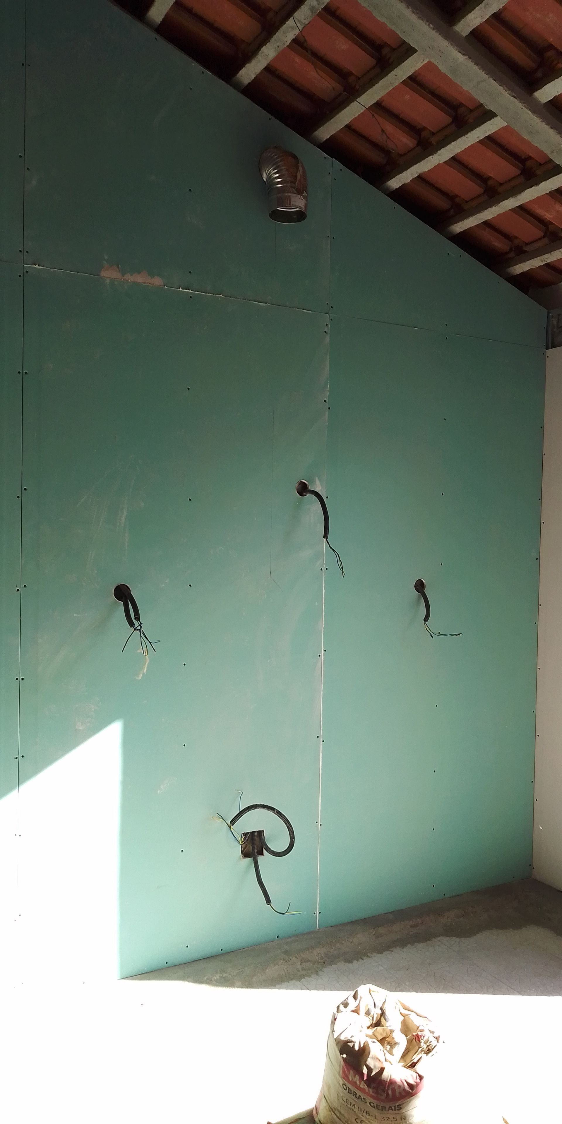 Parede de gesso verde com fios expostos, ventilador de teto e teto inacabado.