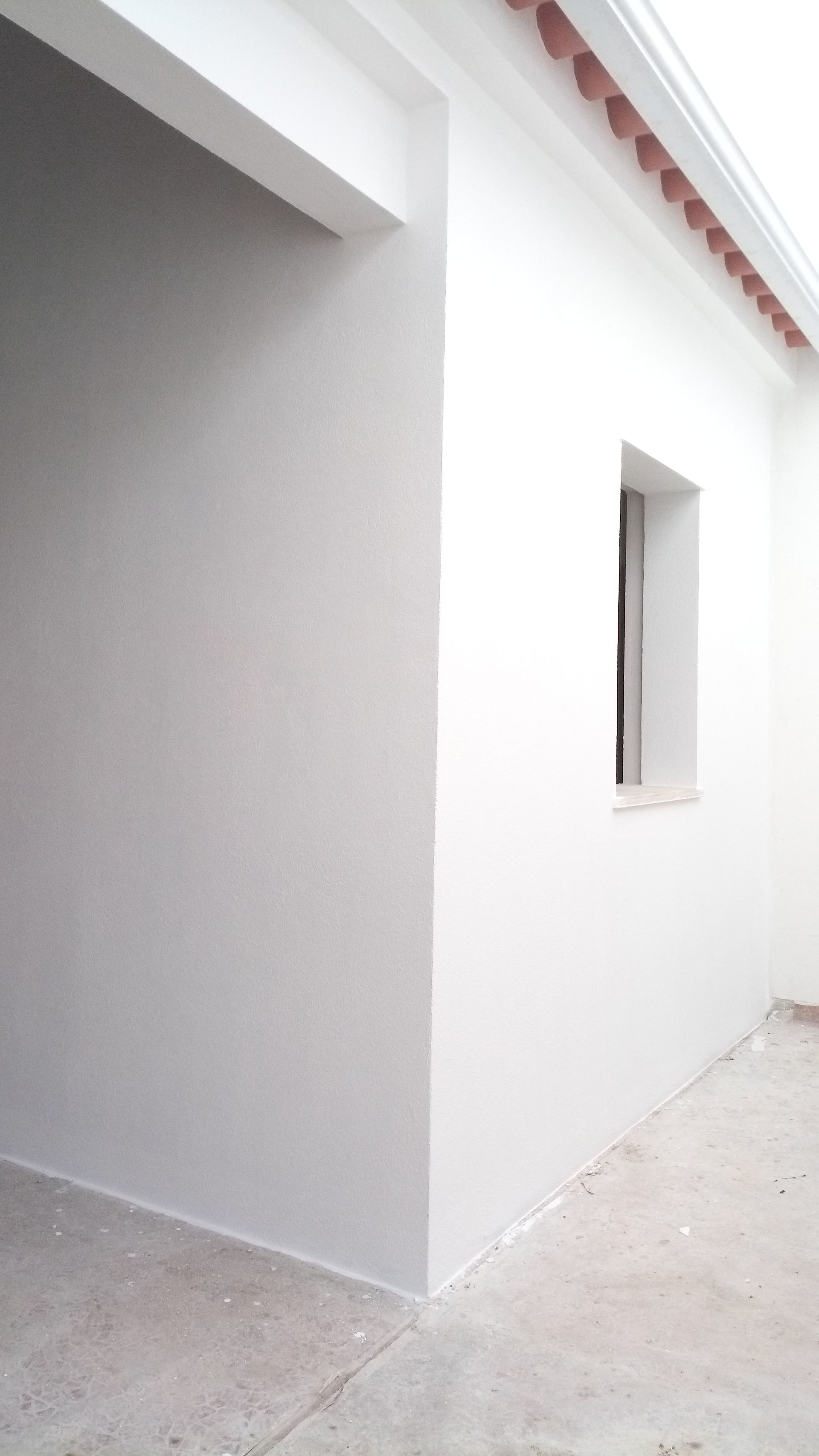 Parede externa de estuque branco com uma pequena janela e uma entrada com passarela coberta.