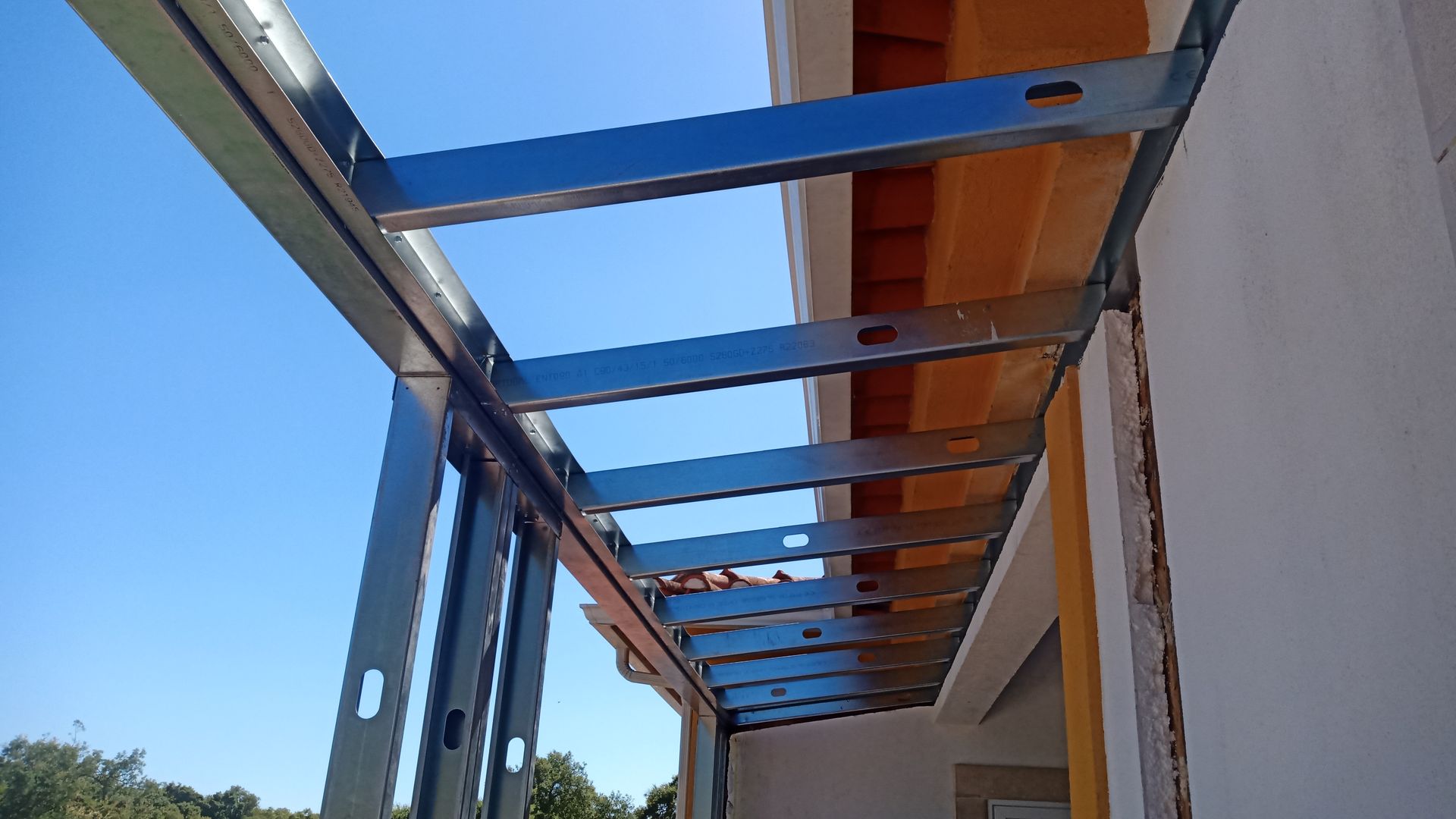 Estrutura metálica, provavelmente para um pátio coberto ou toldo, contra um céu azul.