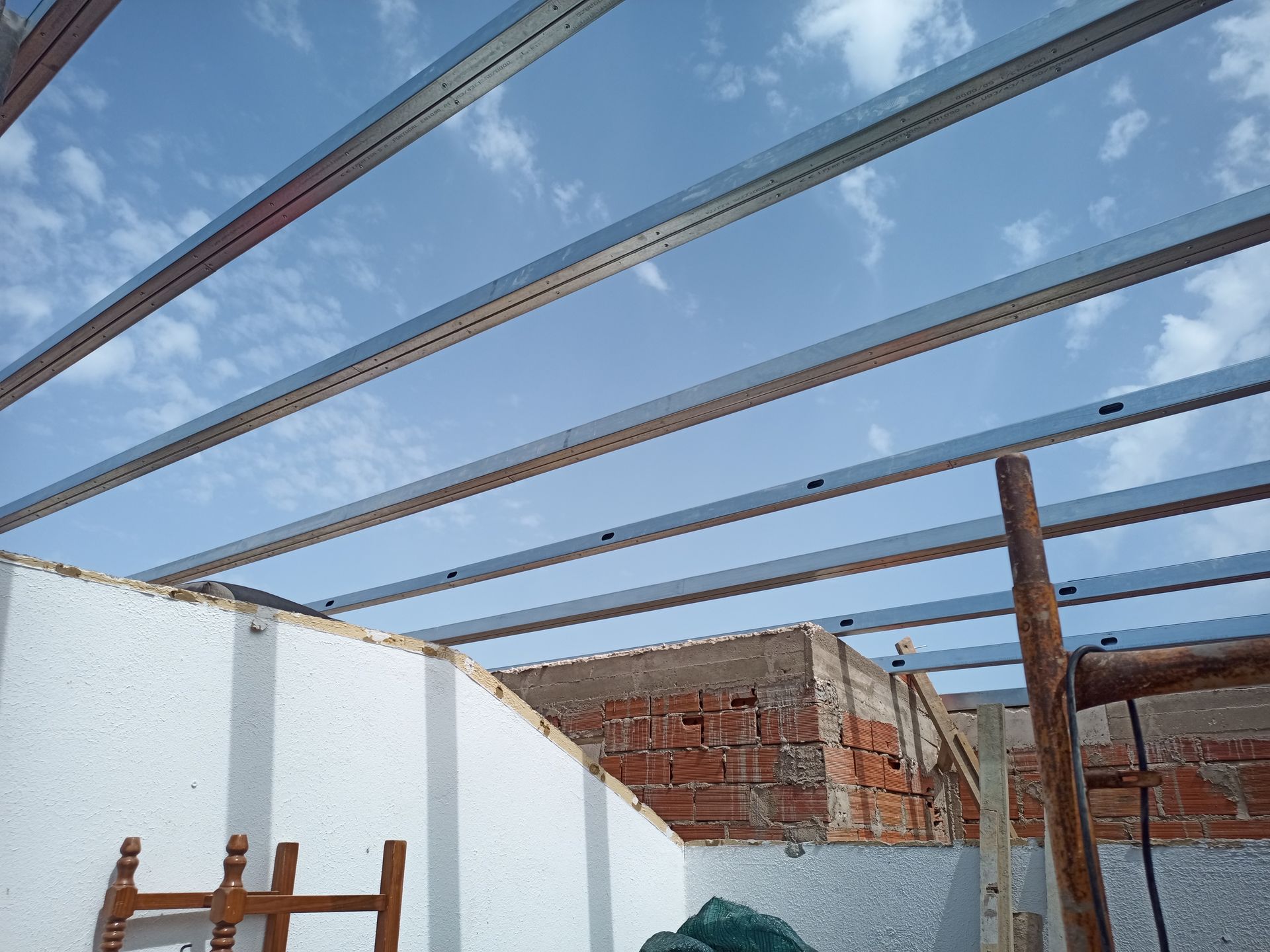 Vigas metálicas instaladas sobre uma estrutura parcialmente construída de tijolos e paredes brancas, tendo como pano de fundo um céu azul.