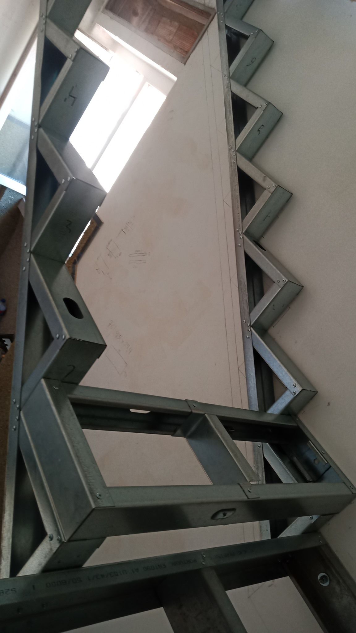 Estrutura metálica para escada contra uma parede branca. Design em ziguezague, construção inacabada.