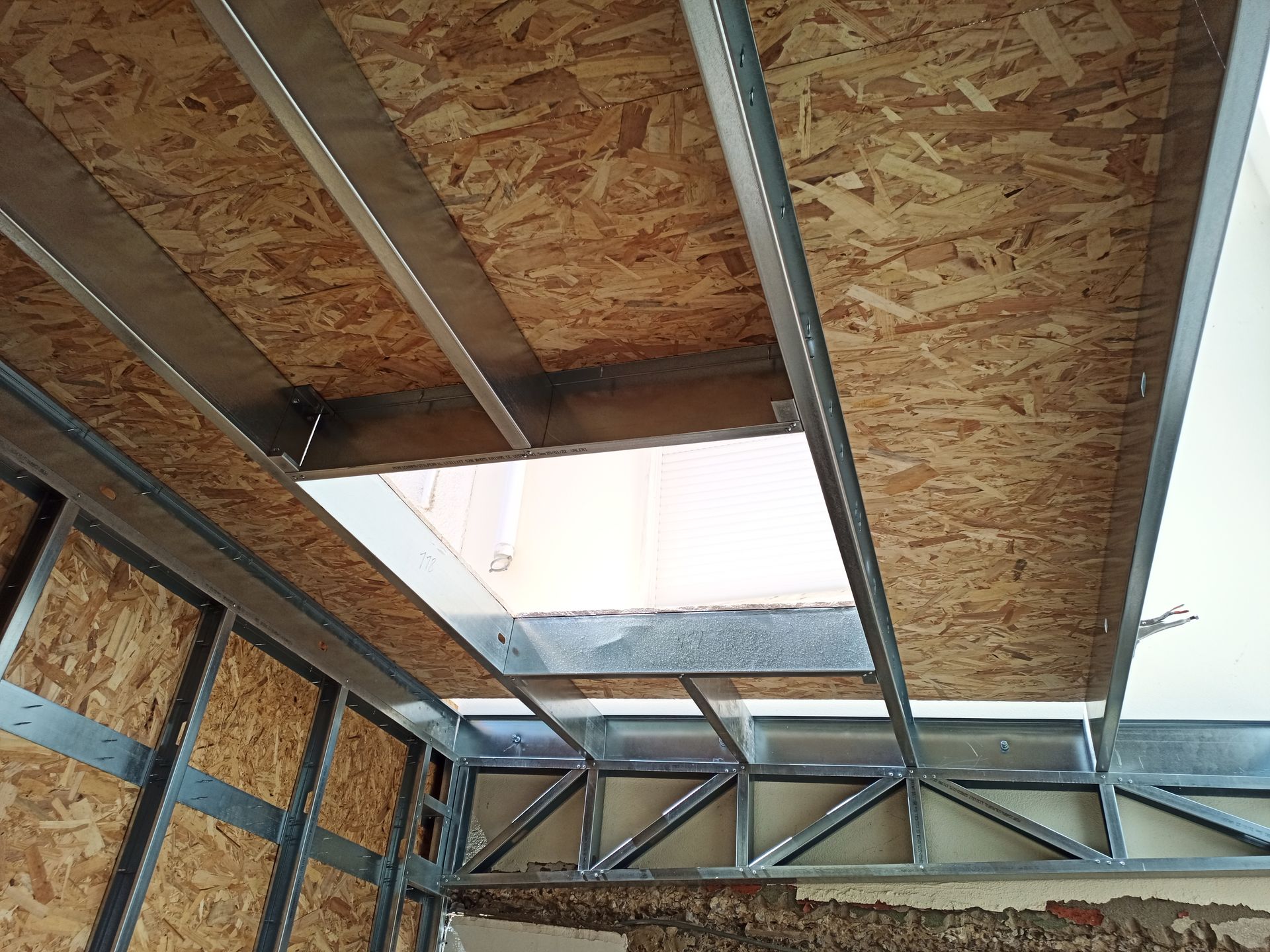 Vista interior de uma sala em construção, com estrutura metálica e painéis de madeira formando as paredes e o teto.