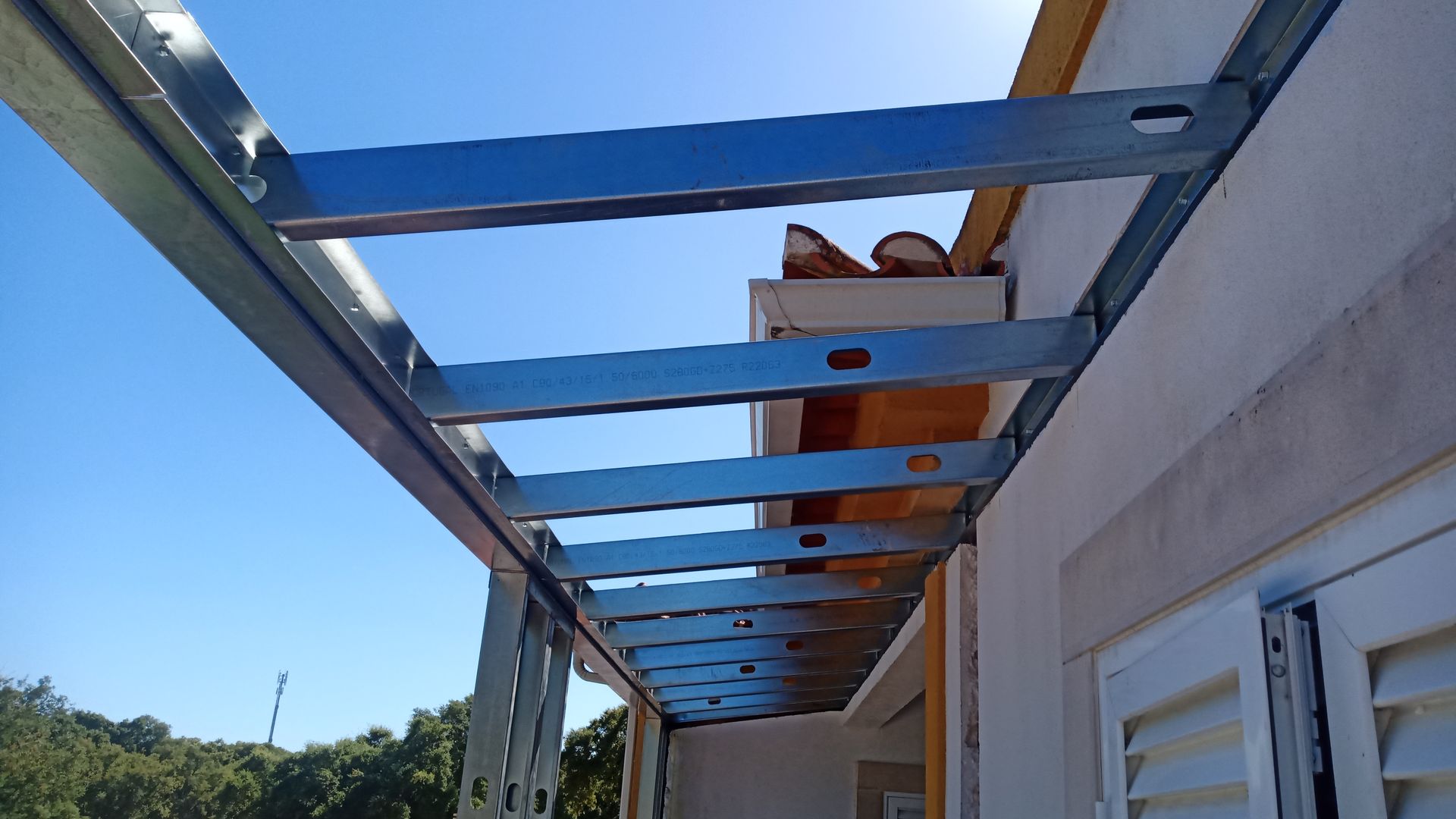 Estrutura metálica para beiral de telhado contra um céu azul brilhante.