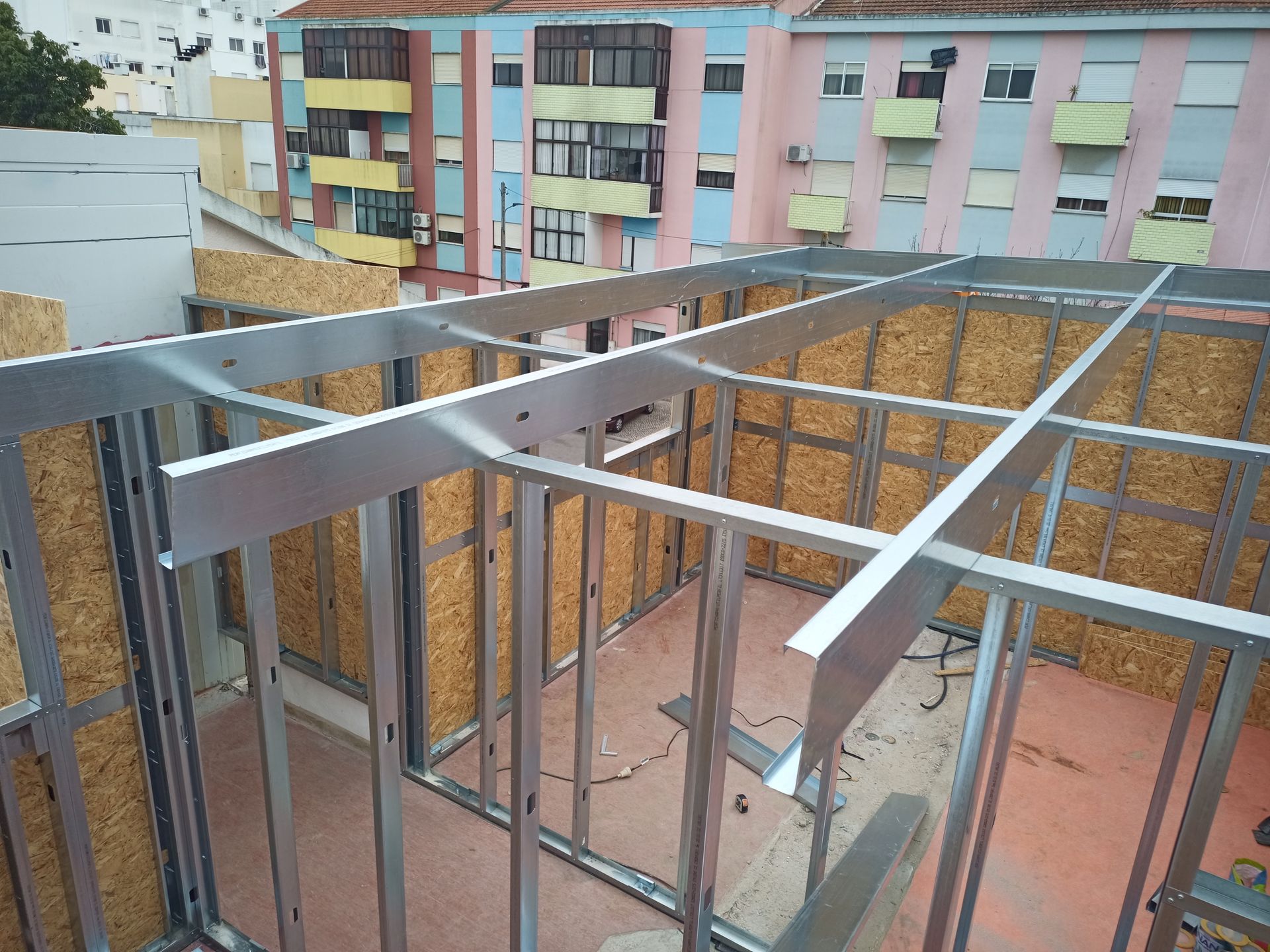 Estrutura metálica de um edifício em construção, vista exterior com edifícios adjacentes ao fundo.