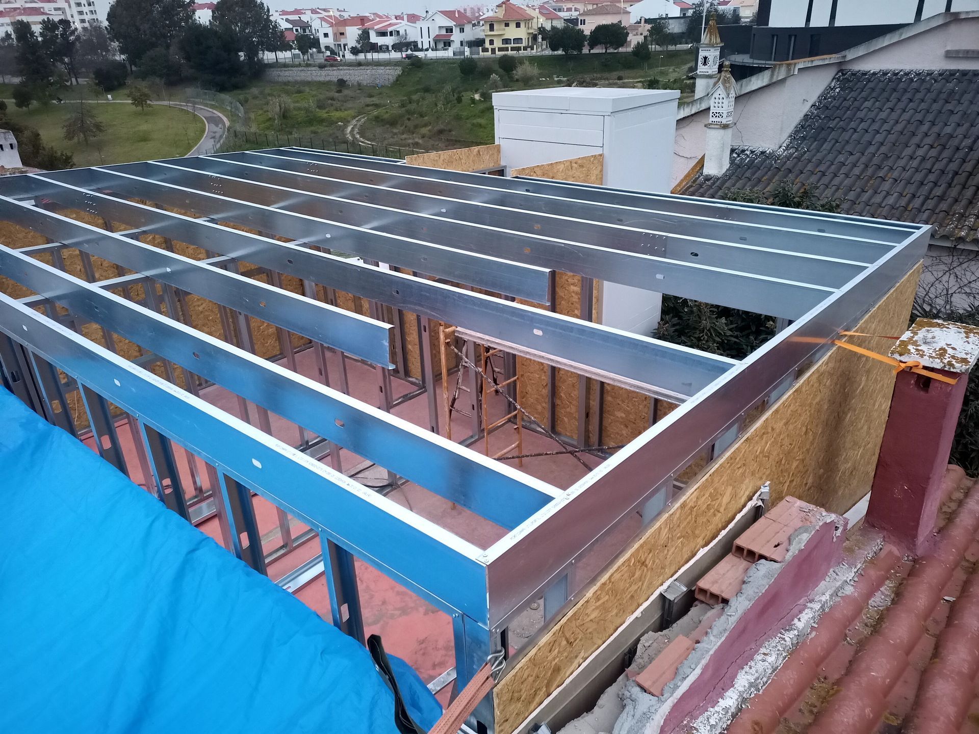 Estrutura metálica de um edifício em construção em um telhado, com a paisagem urbana ao fundo.