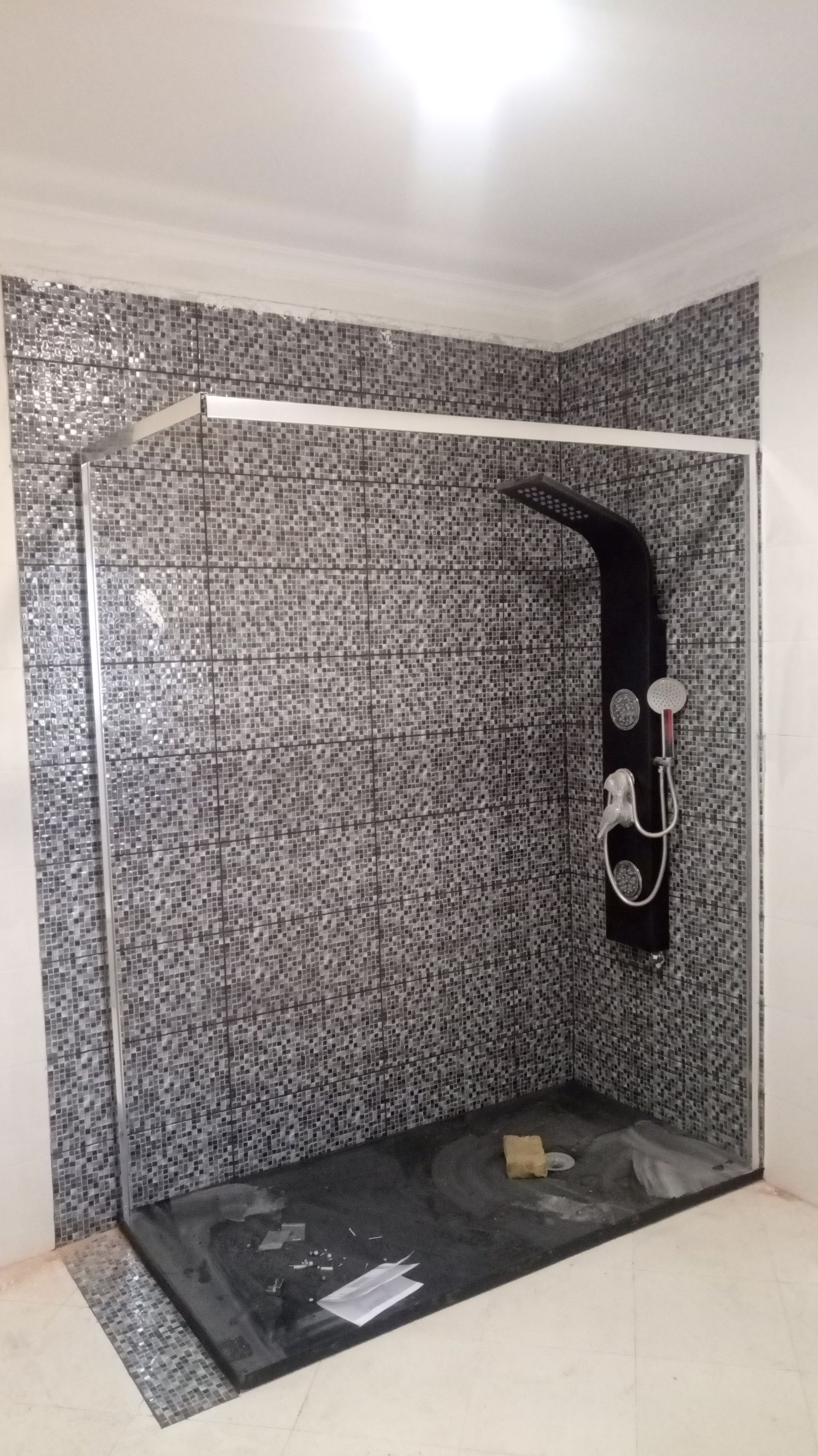 Cabine de duche com paredes revestidas a azulejos de mosaico preto e branco, porta de vidro e painel de duche preto.