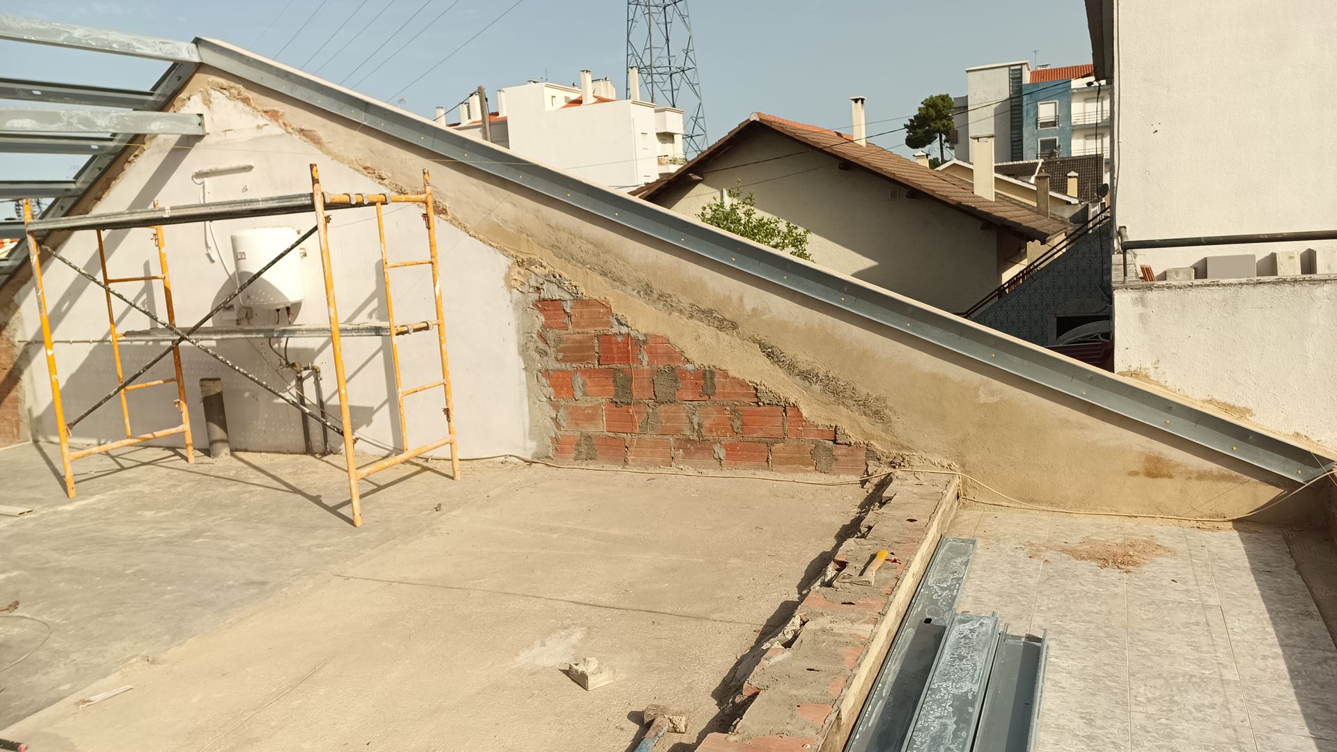 Canteiro de obras: telhado parcialmente construído com tijolos aparentes, vigas metálicas e andaimes.
