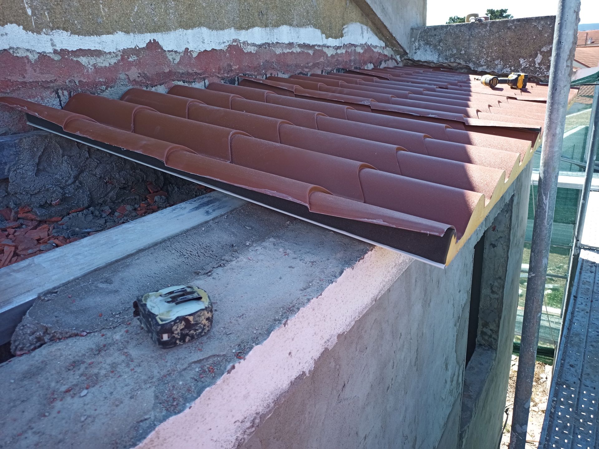 Telhas metálicas marrons sendo instaladas em um prédio, com uma fita métrica na borda da construção.