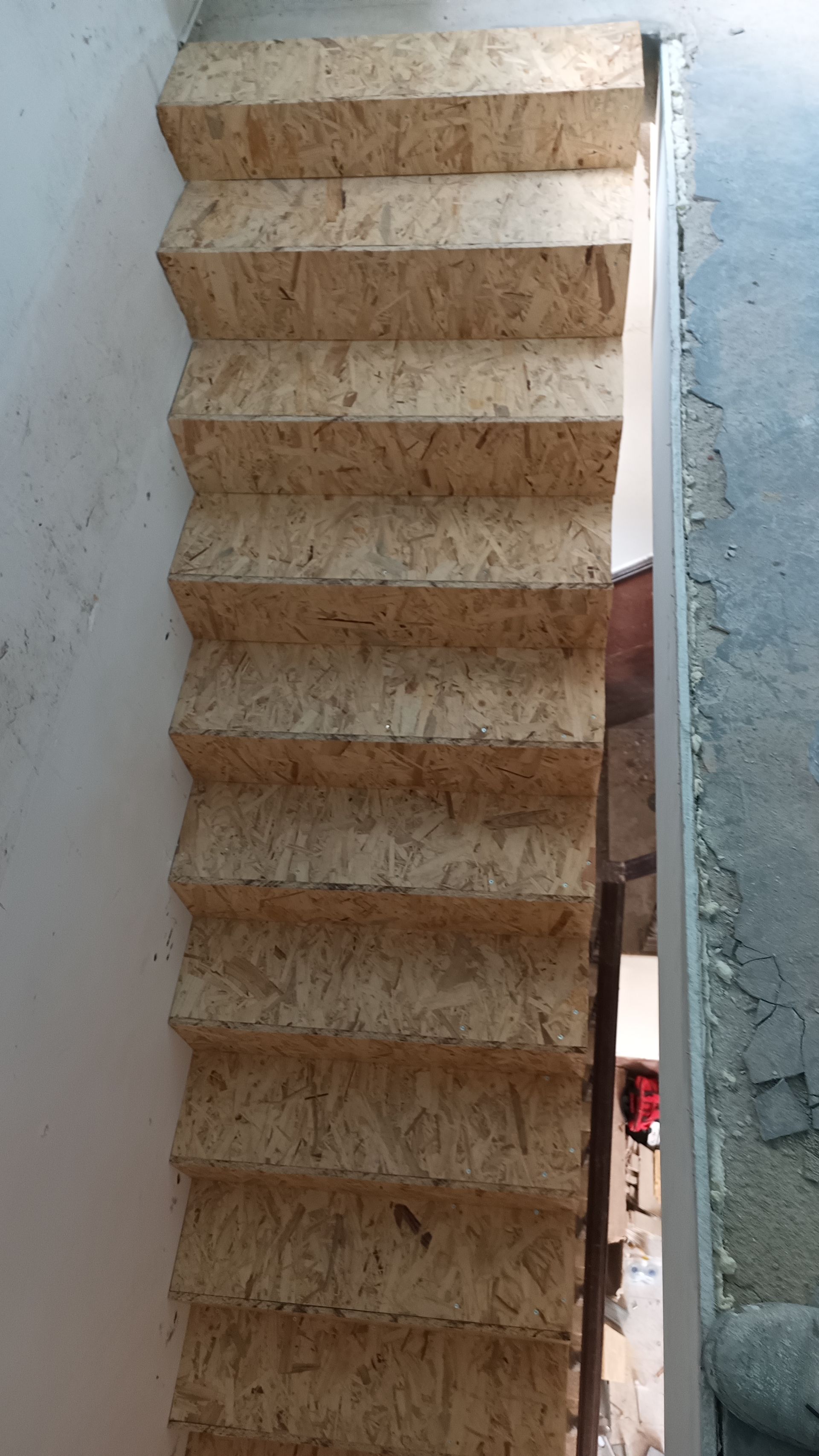 Escada construída com painéis de partículas marrom-claro, que leva ao andar superior através de uma porta.