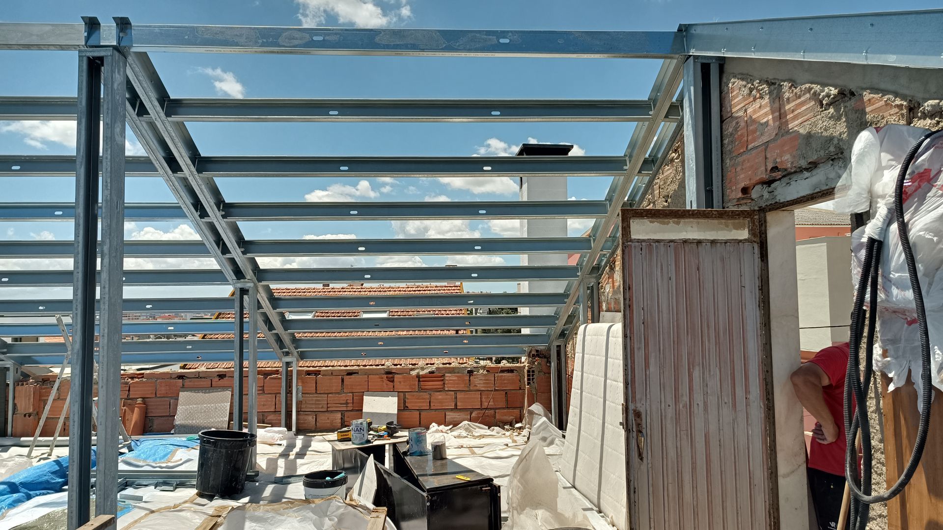 Estrutura metálica de um telhado em construção, visível contra um céu parcialmente nublado.