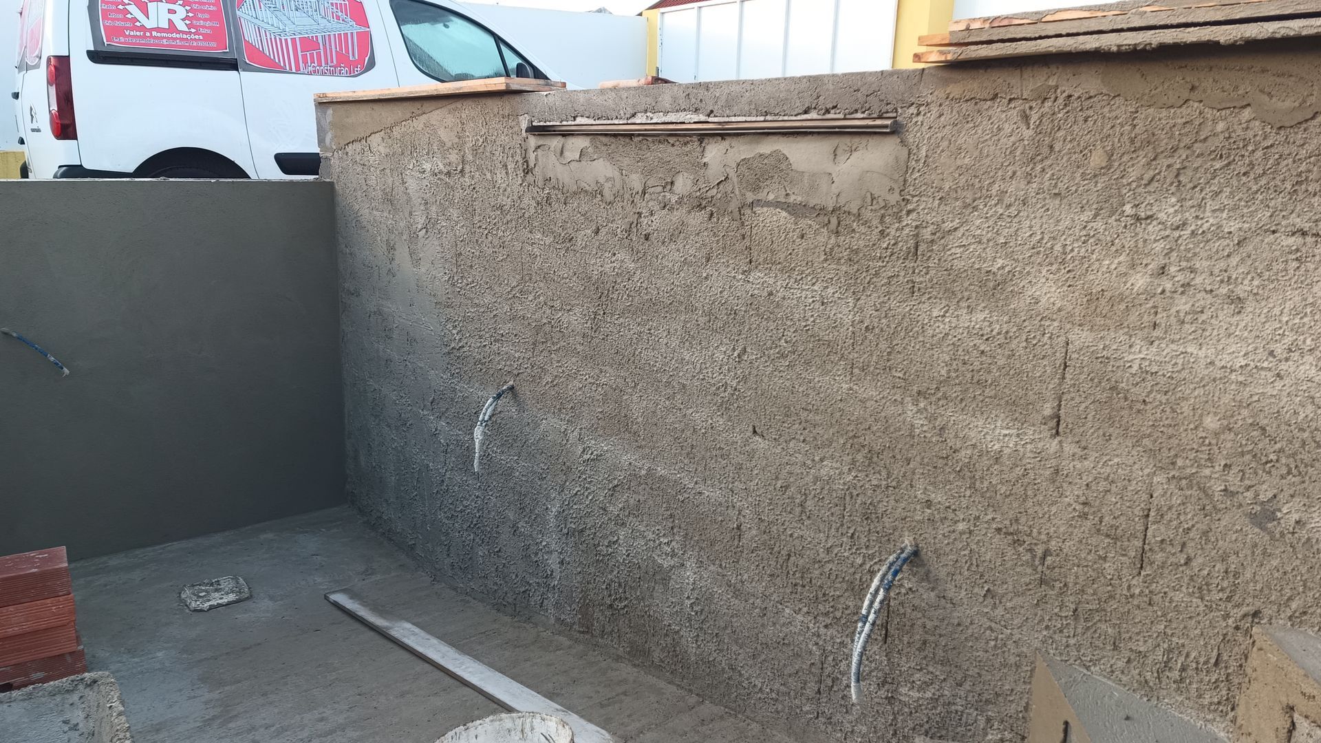 Canteiro de obras com paredes de concreto texturizado, conduítes elétricos e um caminhão de obras ao fundo.