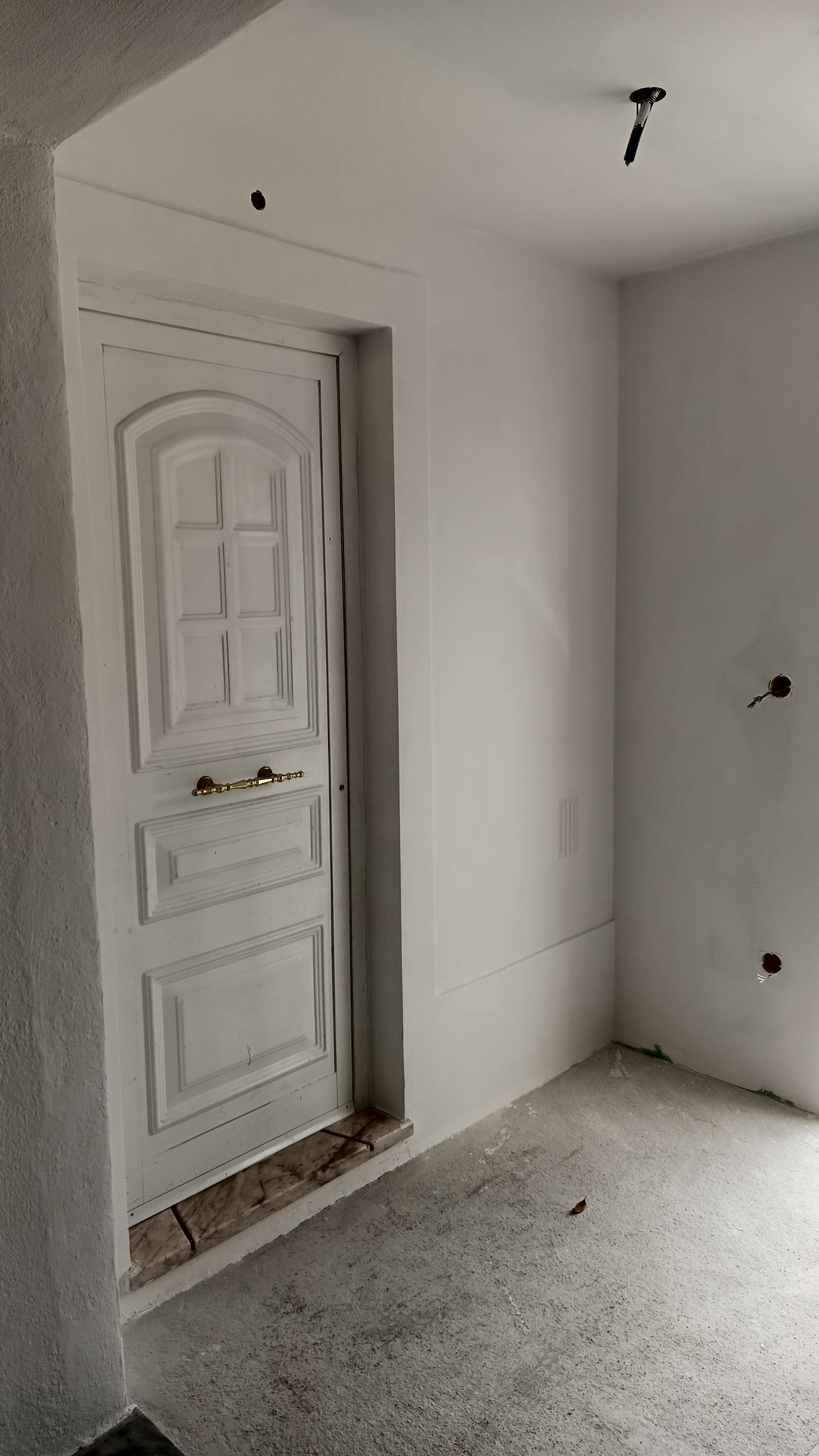 Interior branco com uma porta. Porta branca com painéis. Piso de concreto aparente e paredes brancas.