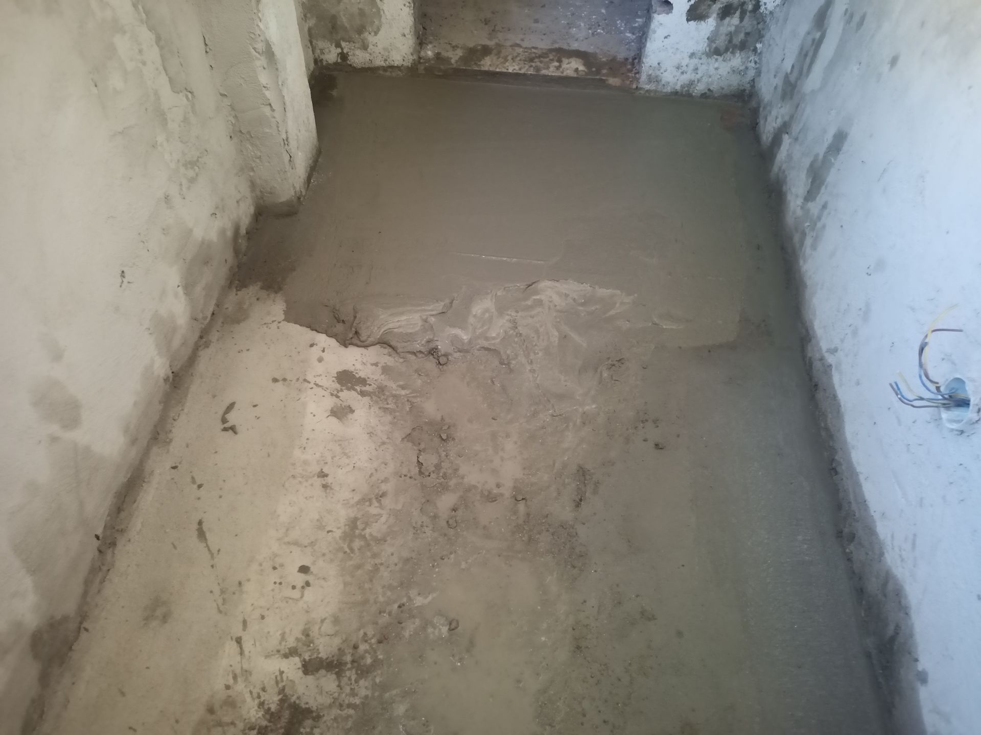 Piso de concreto recém-moldado em um pequeno cômodo inacabado com paredes cinzas.
