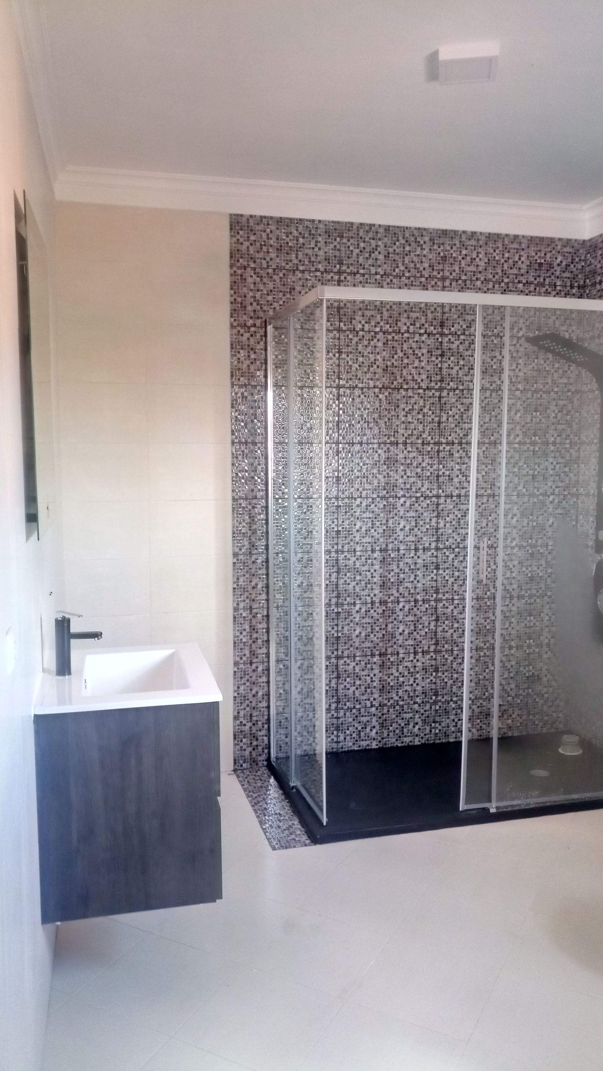 Banheiro moderno com box de vidro, parede revestida com azulejos em mosaico e bancada suspensa.