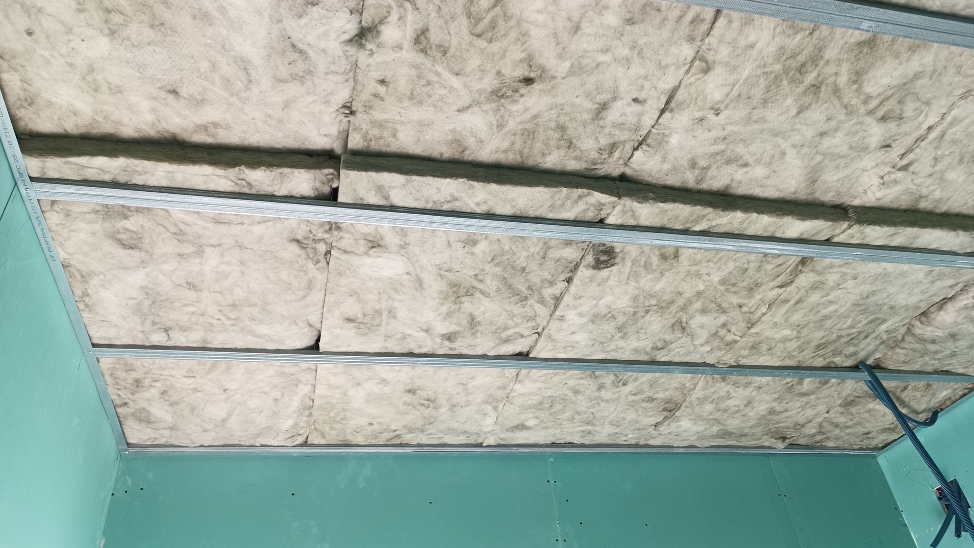 Isolamento do teto entre suportes metálicos em uma sala com paredes verde-claras.