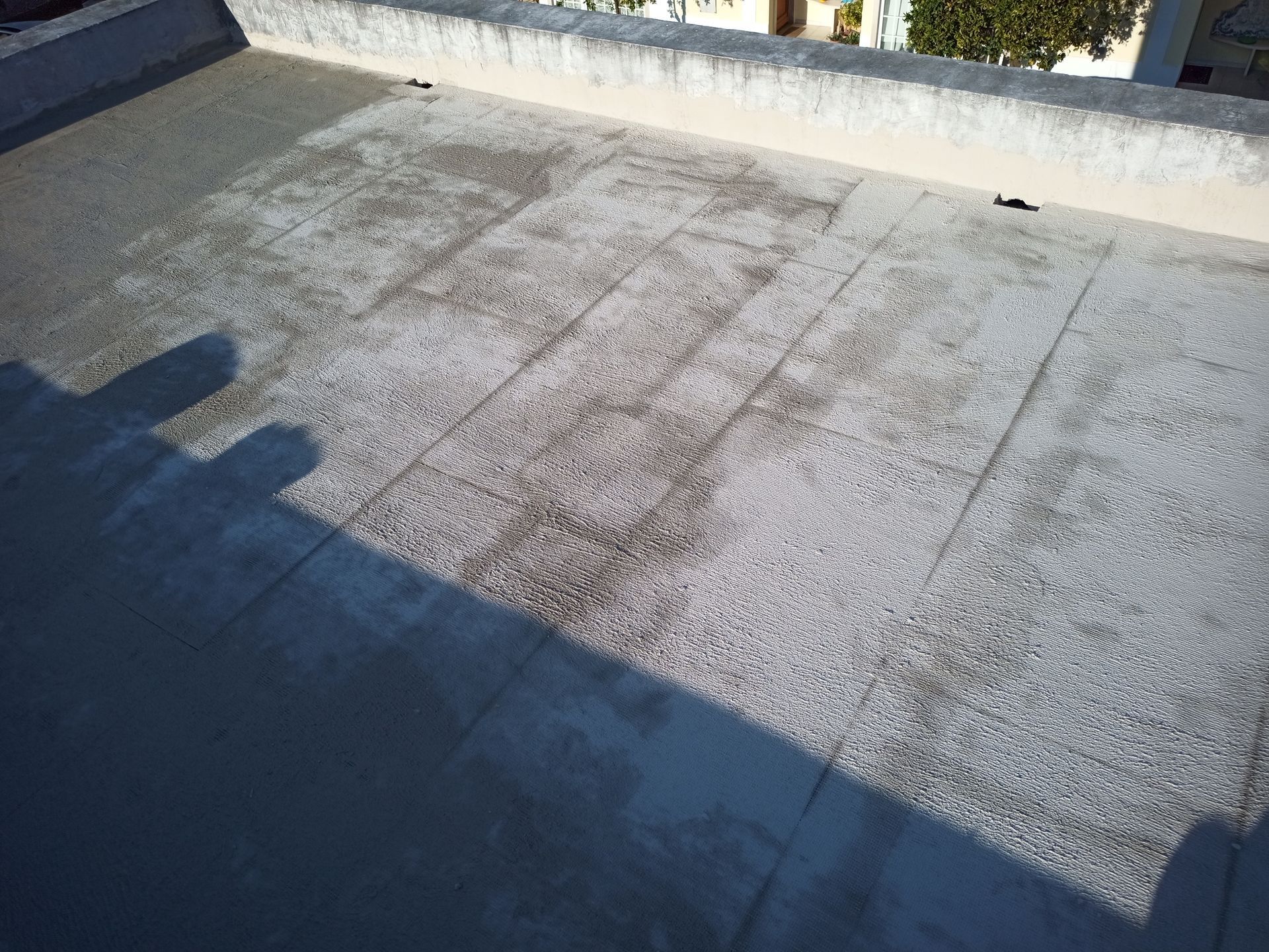 Telhado plano com superfície cinza e esbranquiçada, apresentando desgaste e descoloração, com borda de concreto.